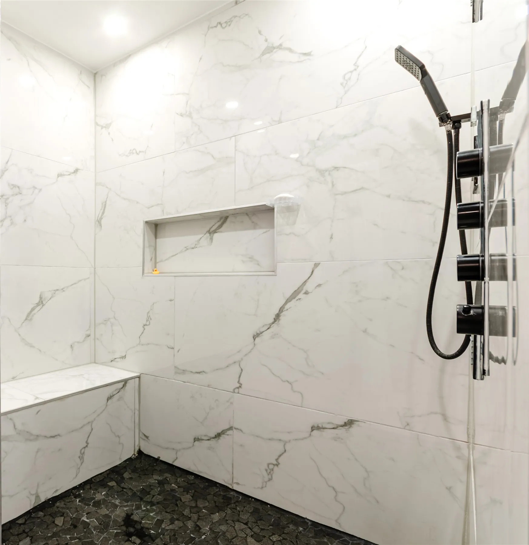 Shower with marbled wall tile, built-in bench, recessed niche, and dark pebble floor tile
