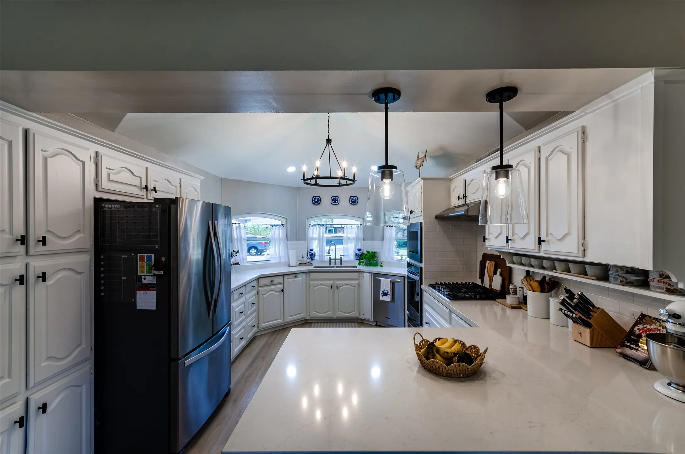 Kitchen featuring white cabinetry with dark hardware, stainless steel refrigerator, stone countertops, and wood-finish flooring