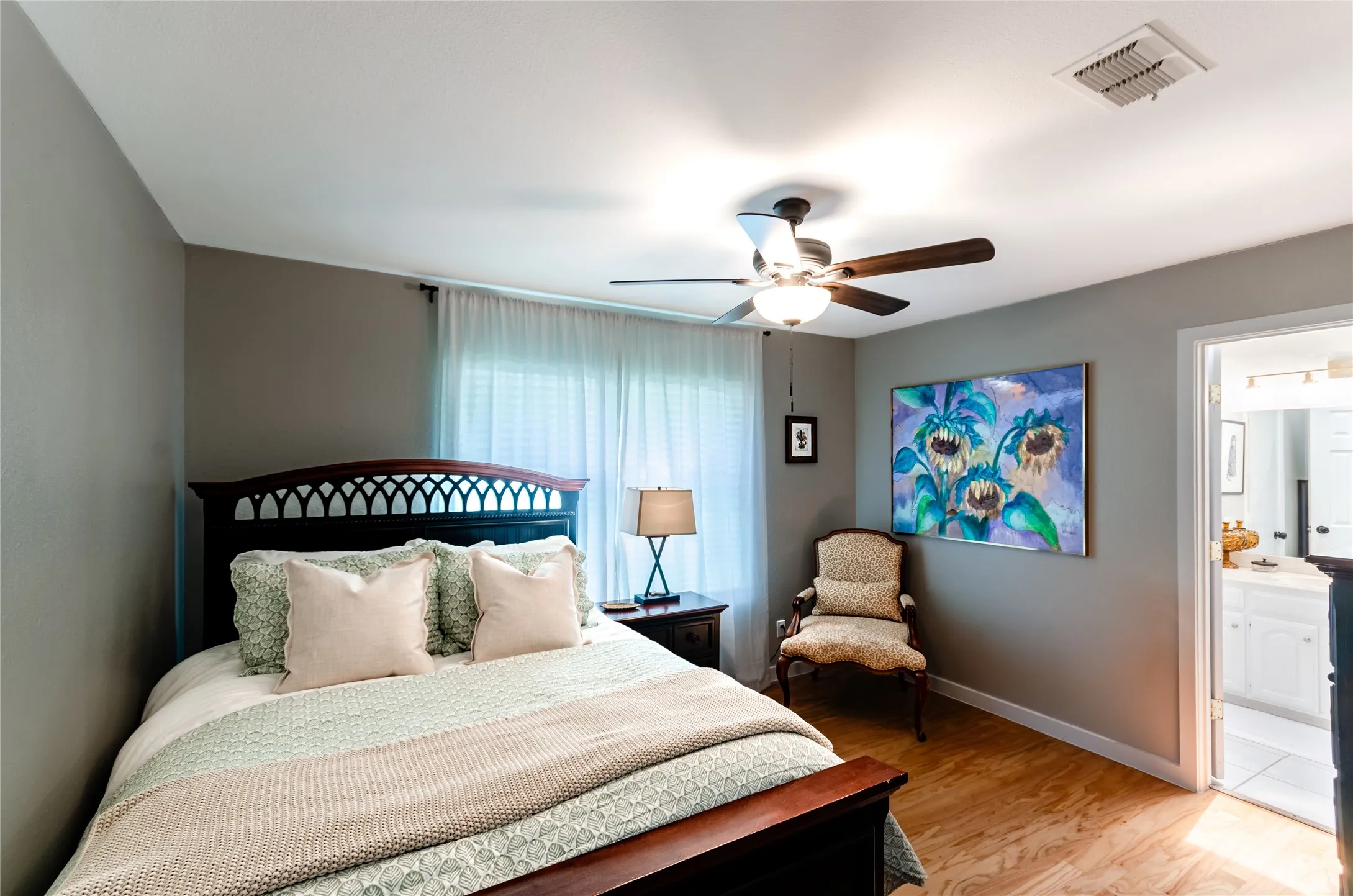 Wood-finish flooring, ceiling fan with integrated lighting, window with sheer curtains, and a doorway opening to an adjacent space