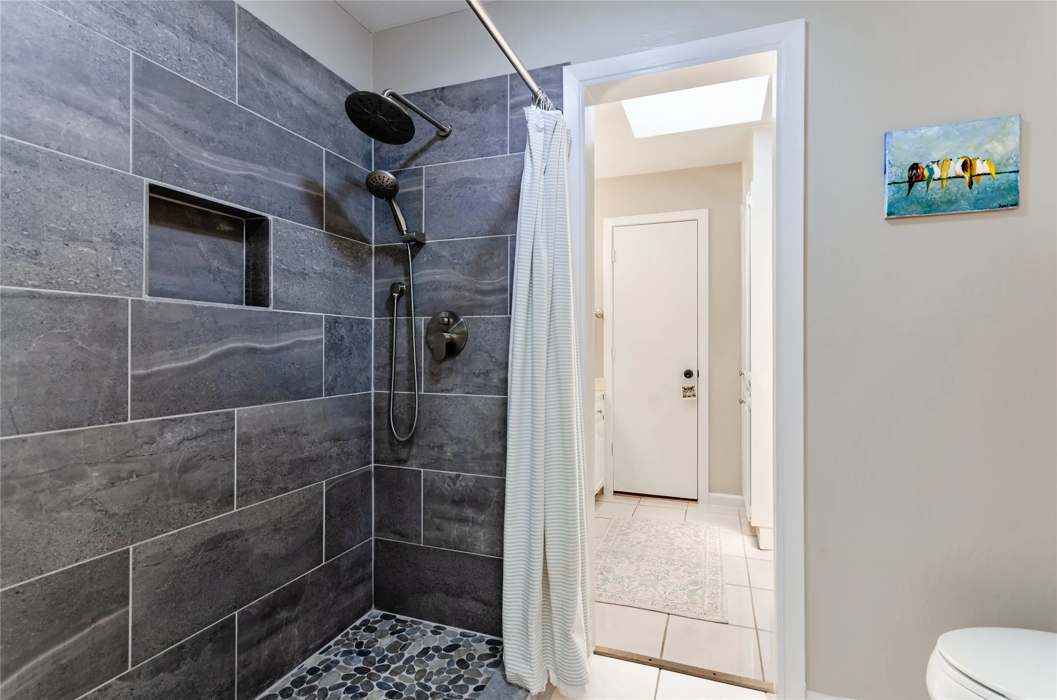 Shower with large format gray wall tile, built-in niche, and river rock flooring