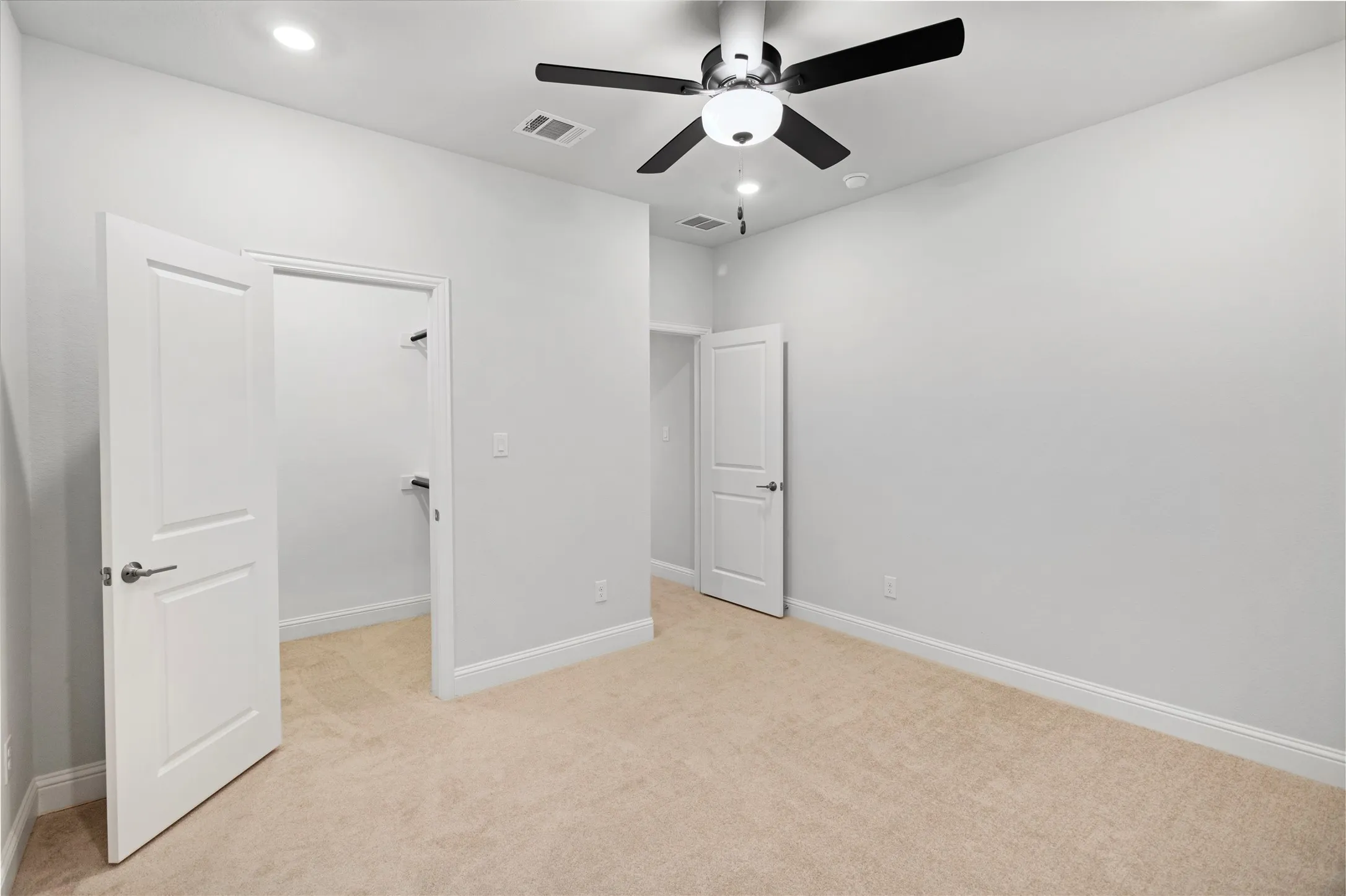 Bright, open bedroom featuring neutral wall finishes, warm wood-finish flooring, and abundant natural light from recessed ceiling fixtures