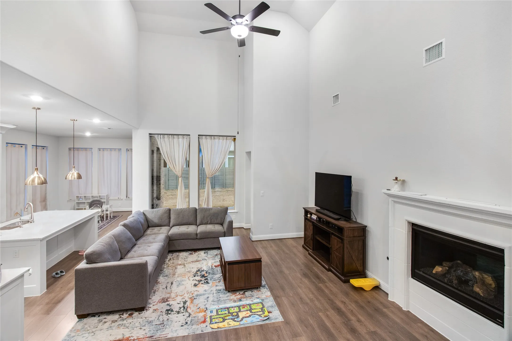 Open-concept living space featuring soaring ceilings with ceiling fan, wood-finish flooring throughout, and a gas fireplace with surround