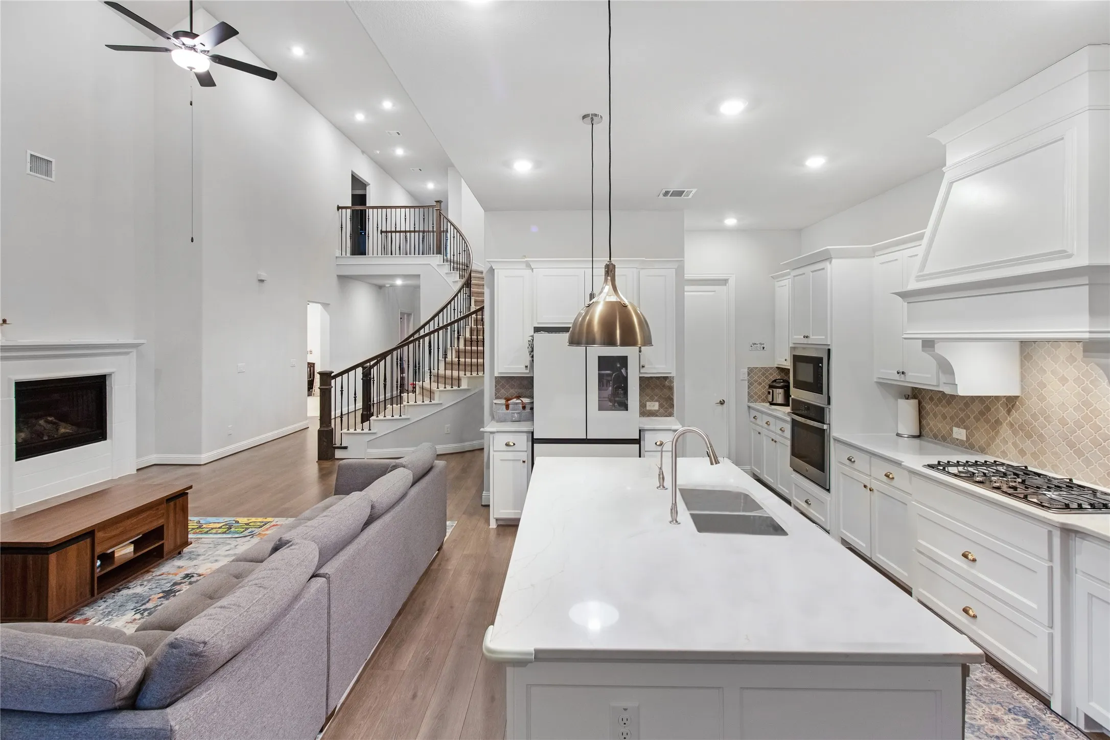 Open-concept living and dining space featuring a white kitchen with gas cooktop, stainless steel appliances, white cabinetry, and a quartz waterfall island