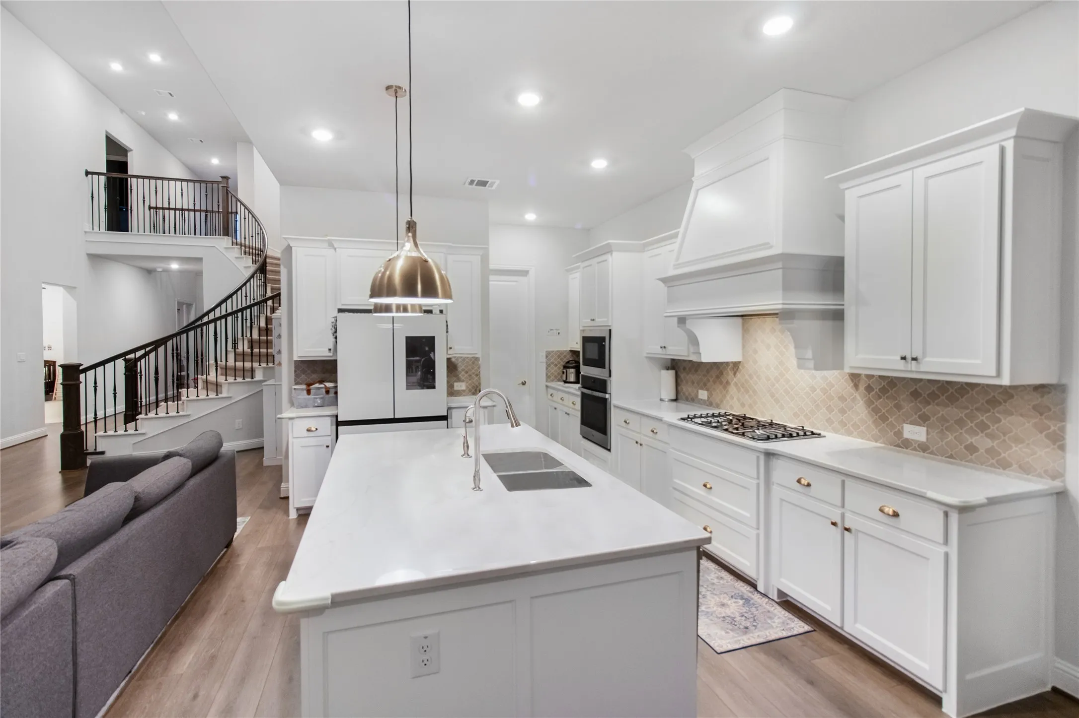 Contemporary kitchen featuring white cabinetry, a large center island with white quartz countertop, stainless steel appliances including a gas cooktop and built-in refrigerator, pendant lighting, and subway tile backsplash