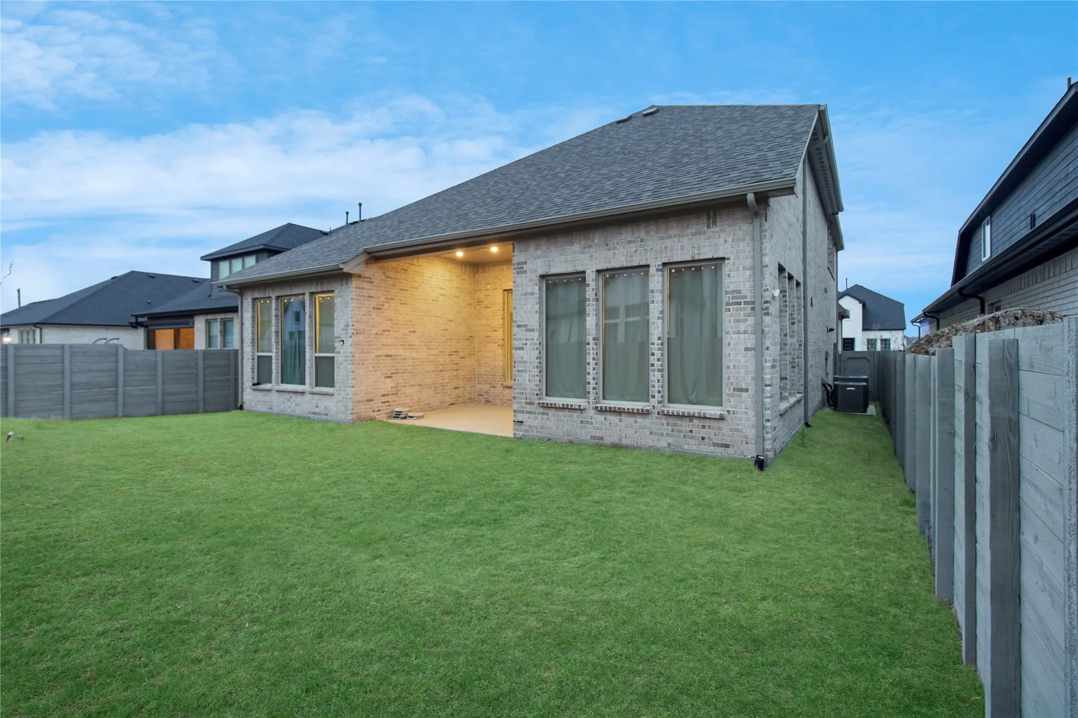 Expansive green lawn with a covered patio featuring recessed lighting