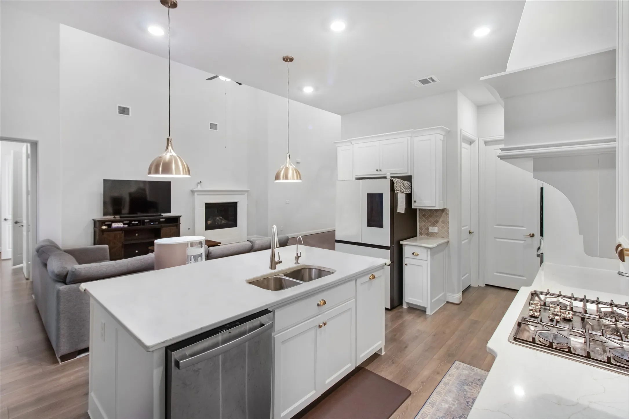 Contemporary kitchen and living spaces featuring white cabinetry, quartz countertops, and stainless steel appliances including a gas cooktop and built-in refrigerator