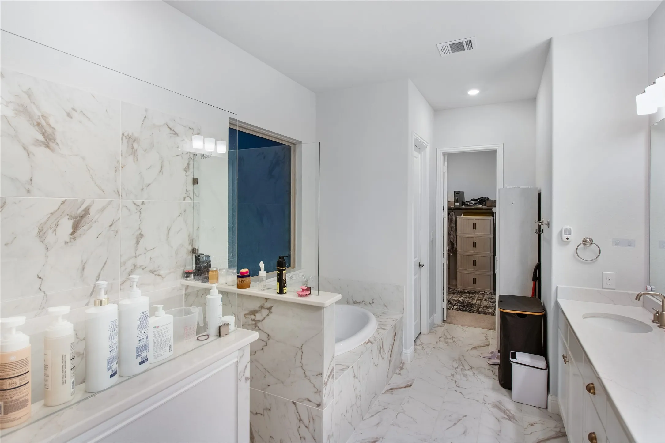 Spacious bathroom featuring a built-in soaking tub, a dual vanity with undermount sinks, and marble-look tile flooring