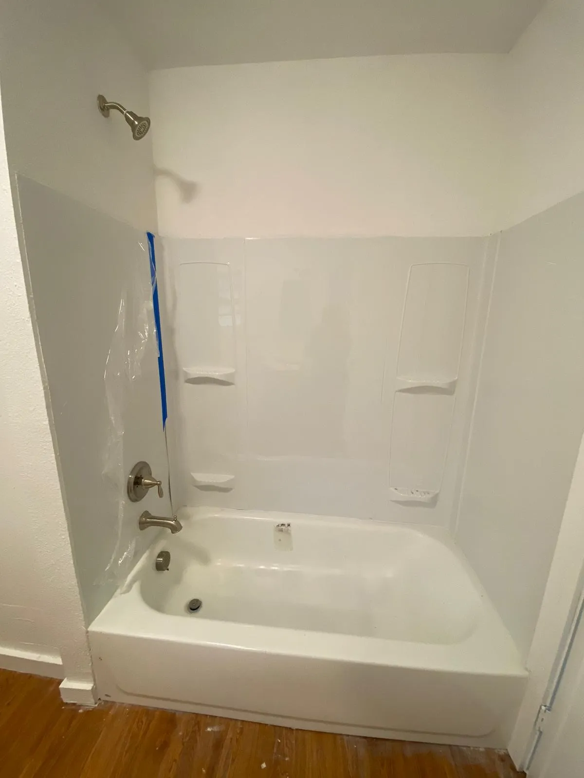 White acrylic bathtub with integrated shelving, brushed nickel fixtures, and a shower head