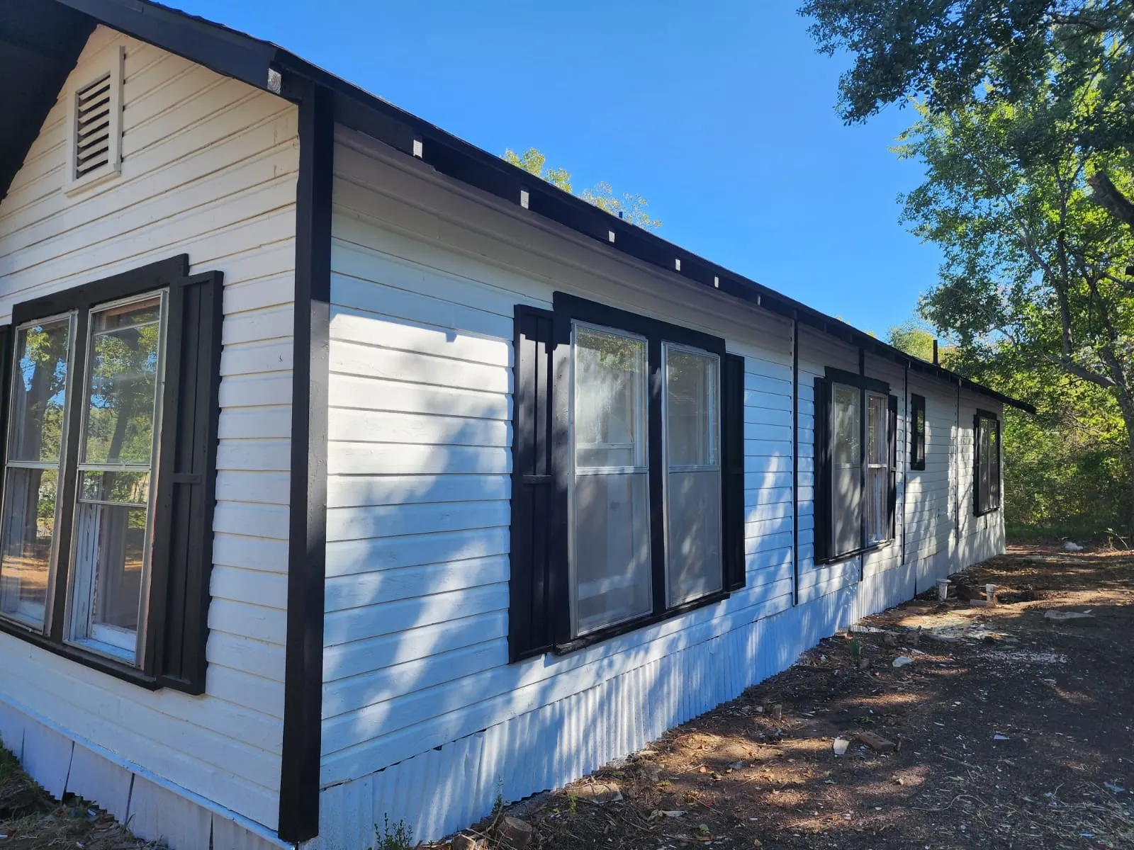 White horizontal siding exterior with black trim, multiple windows with black shutters, and a slatted gable vent