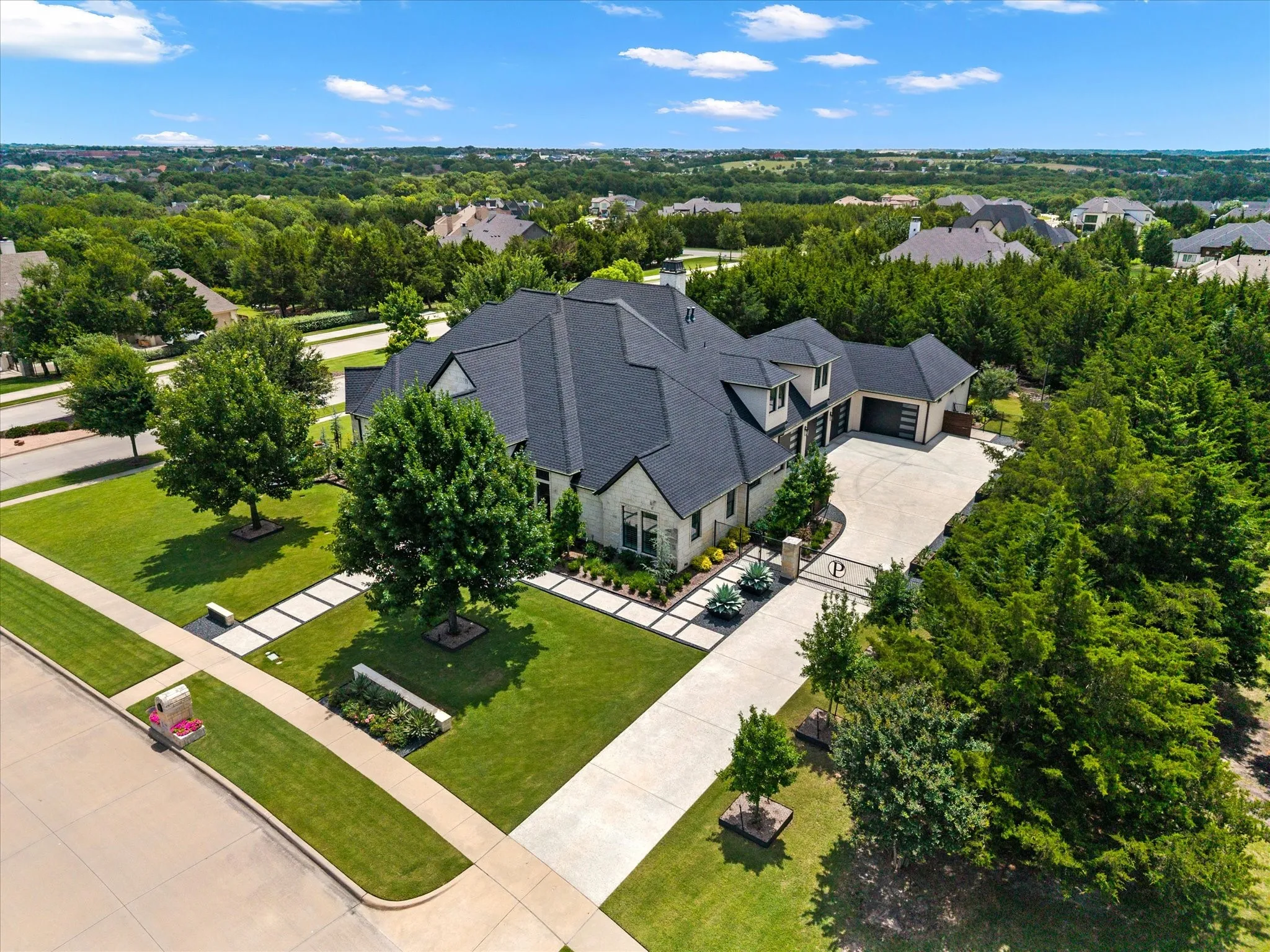 Expansive property featuring a multi-gabled roofline, light-toned brick exterior, a substantial paved driveway, and mature landscaping with established trees