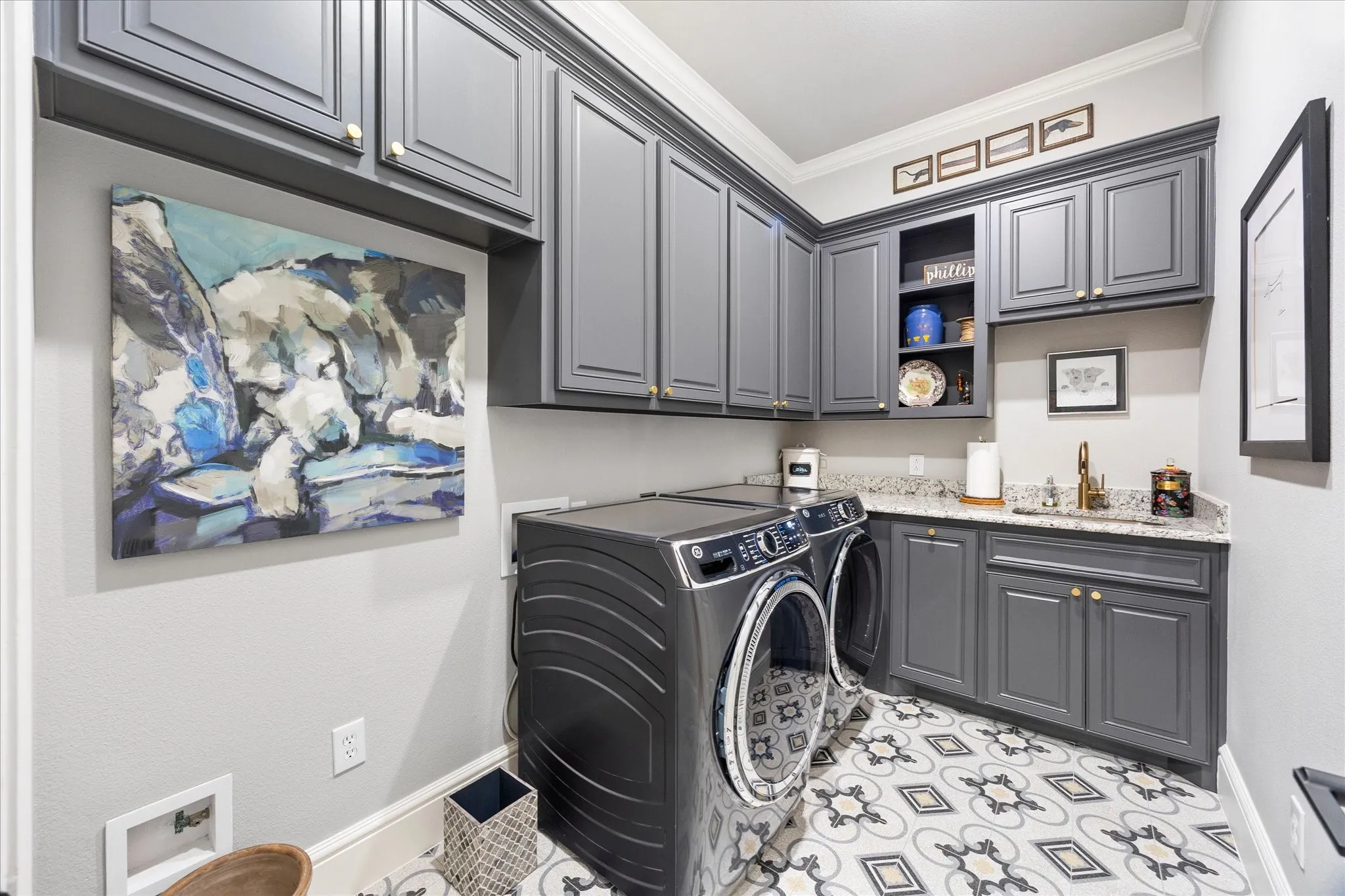 Gray shaker-style cabinetry with gold-tone hardware, light-toned countertop, undermount sink with gold-tone faucet, and patterned tile flooring