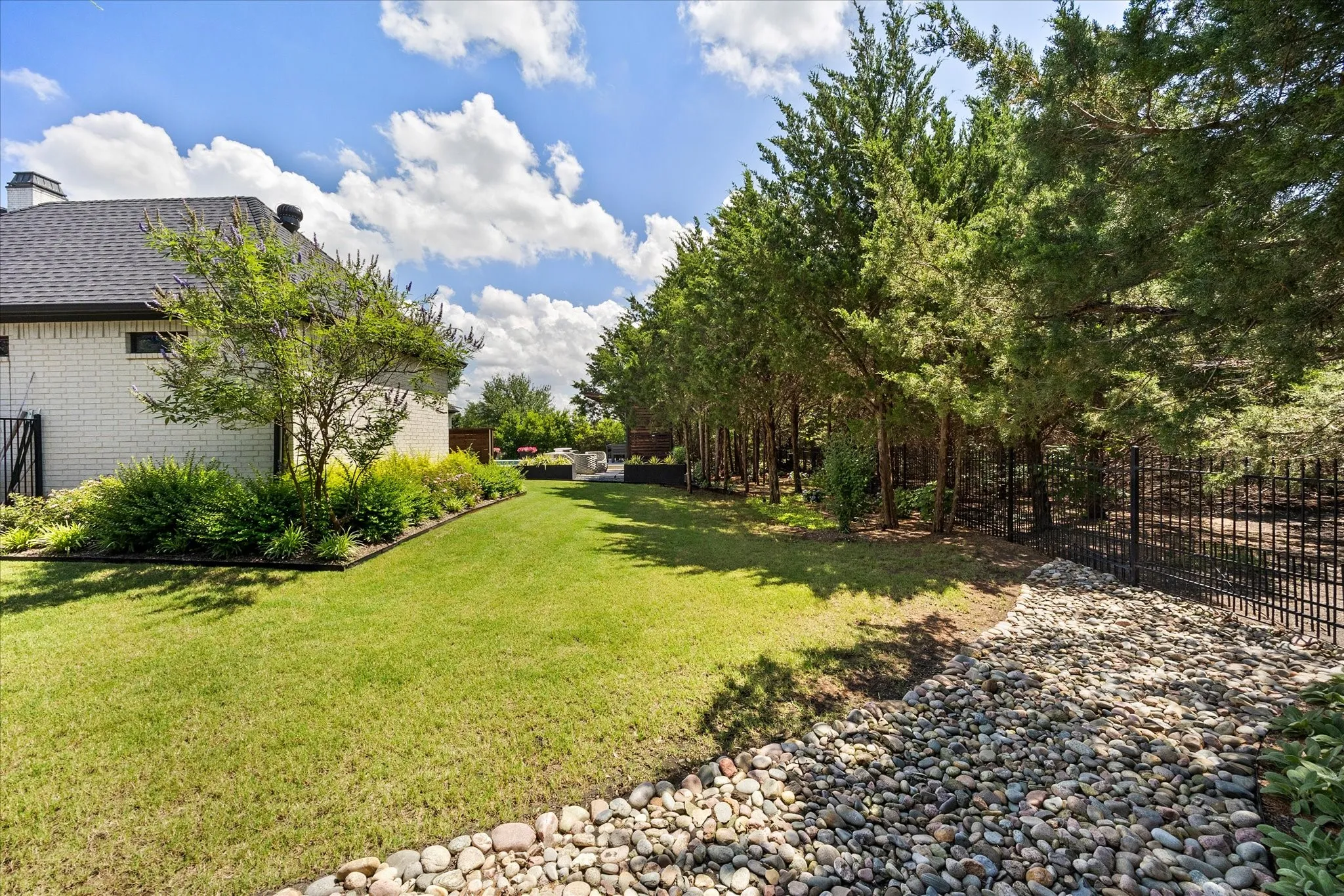 Expansive green lawn, mature trees, white brick exterior, black roof, and decorative stone landscaping