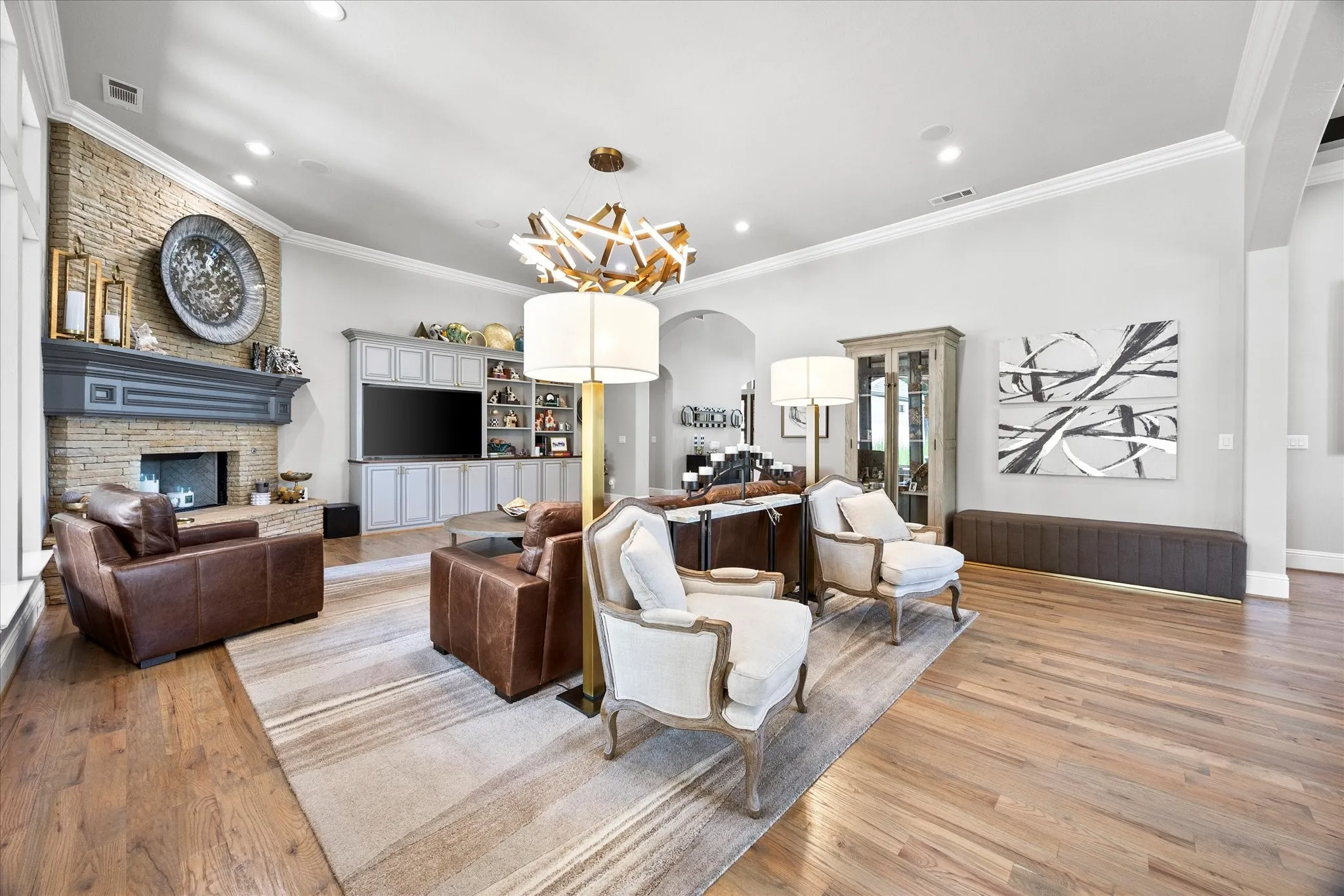 Hardwood flooring throughout, stone-clad fireplace with mantel, built-in media cabinetry, recessed lighting, and a decorative ceiling fixture