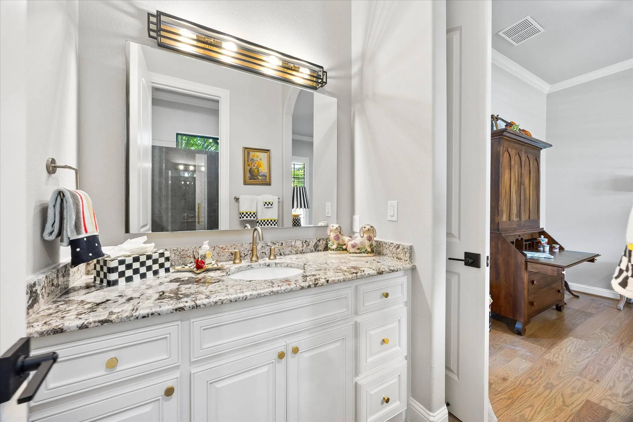 White vanity with gold-tone hardware, granite countertop, undermount sink, and wall-mounted light fixture
