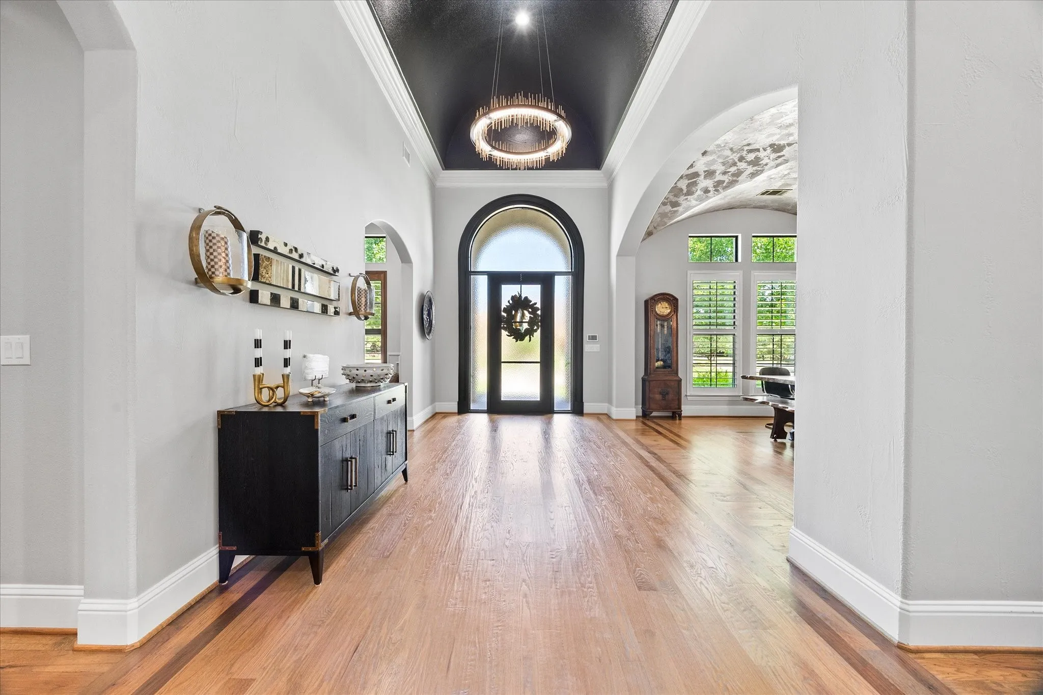 Hardwood flooring, arched doorway, vaulted ceiling with chandelier, arched windows with plantation shutters, and textured barrel-vaulted ceiling