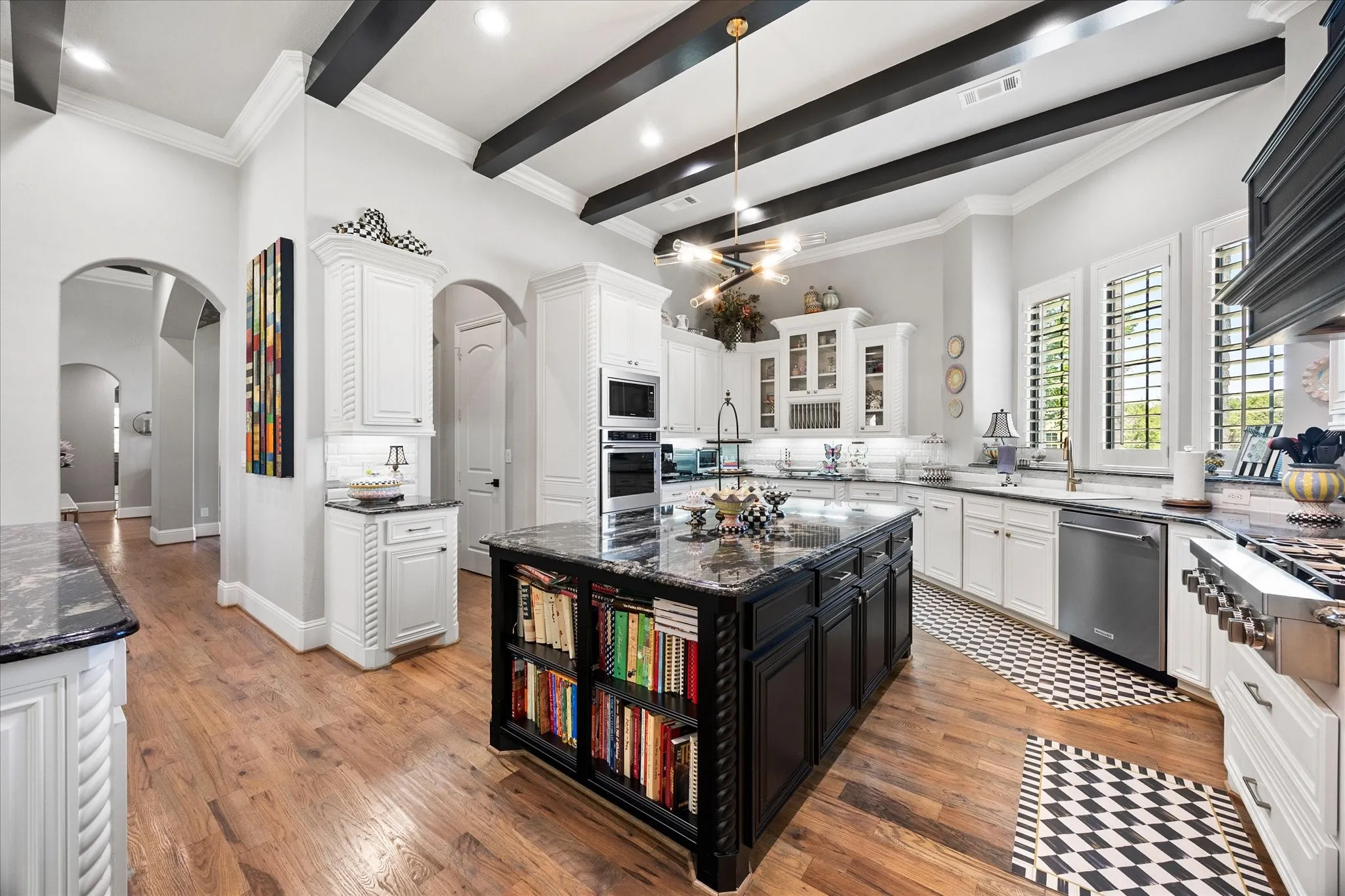 Kitchen featuring vaulted ceilings with exposed beams, wood-finish flooring, custom white cabinetry, a large central island with built-in shelving, and stainless steel appliances