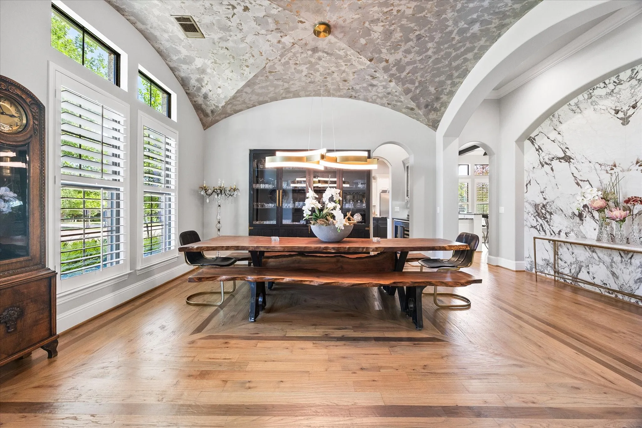 Barrel vault ceiling, hardwood flooring with decorative inlay, arched wall opening with stone accent wall, white plantation shutters, and a built-in display cabinet