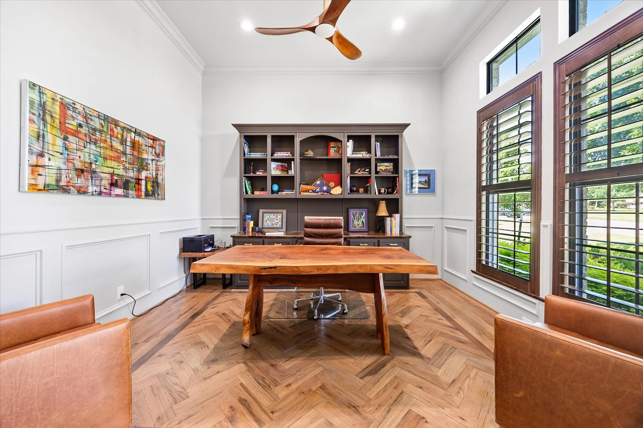 Herringbone wood-finish flooring, built-in shelving, crown molding, wainscoting, and tall windows with plantation shutters