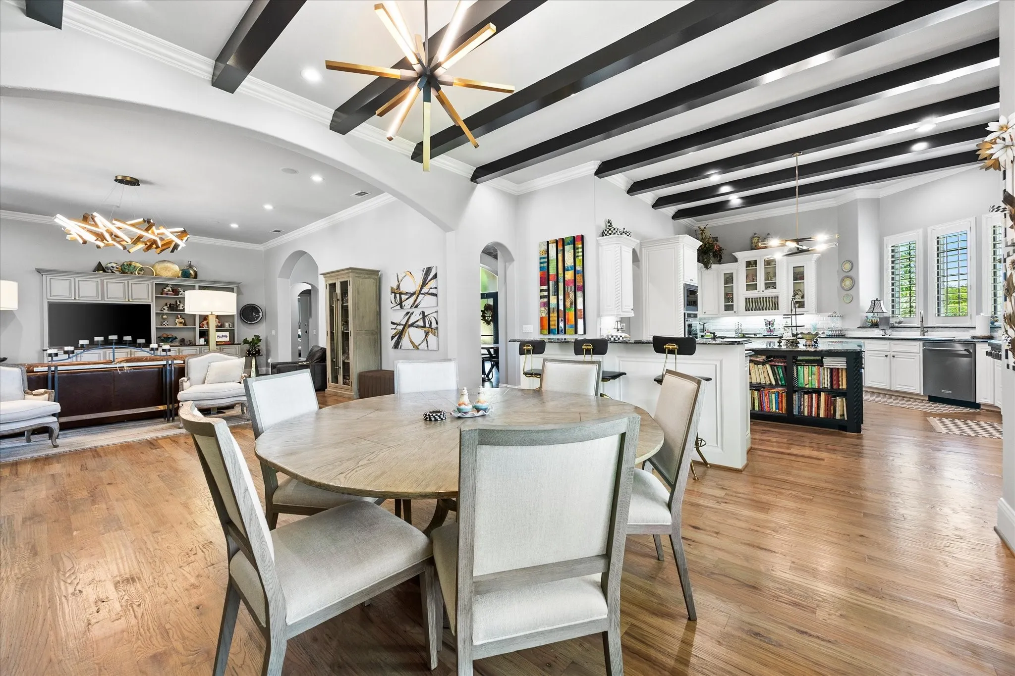 Open concept living space featuring wood-finish flooring, exposed ceiling beams, built-in cabinetry, an island with integrated shelving, and stainless steel appliances