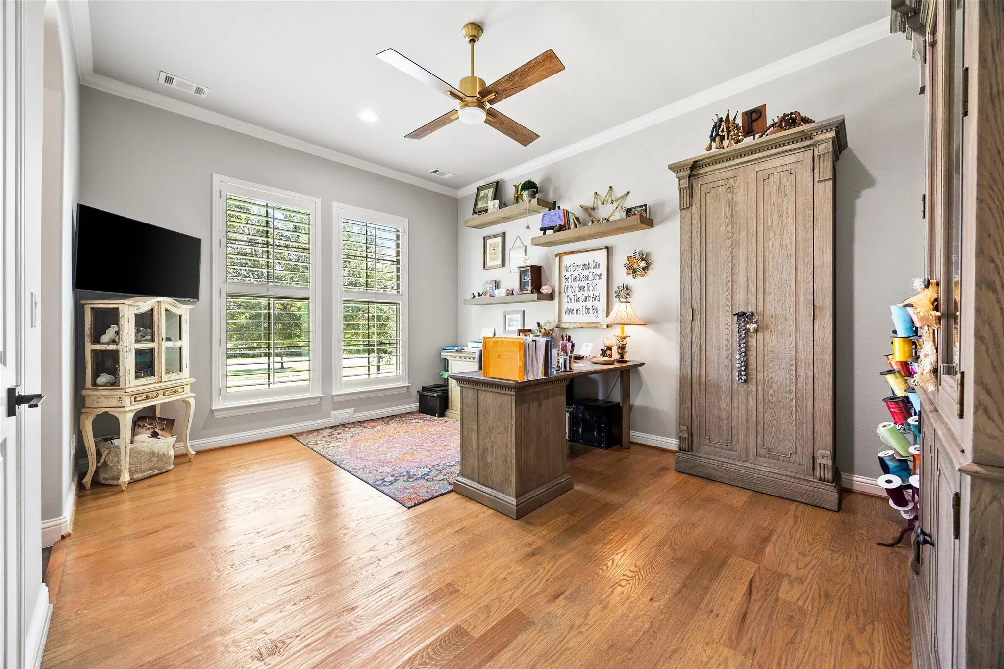 Hardwood flooring, painted walls, crown molding, double windows with plantation shutters, and a ceiling fan with light