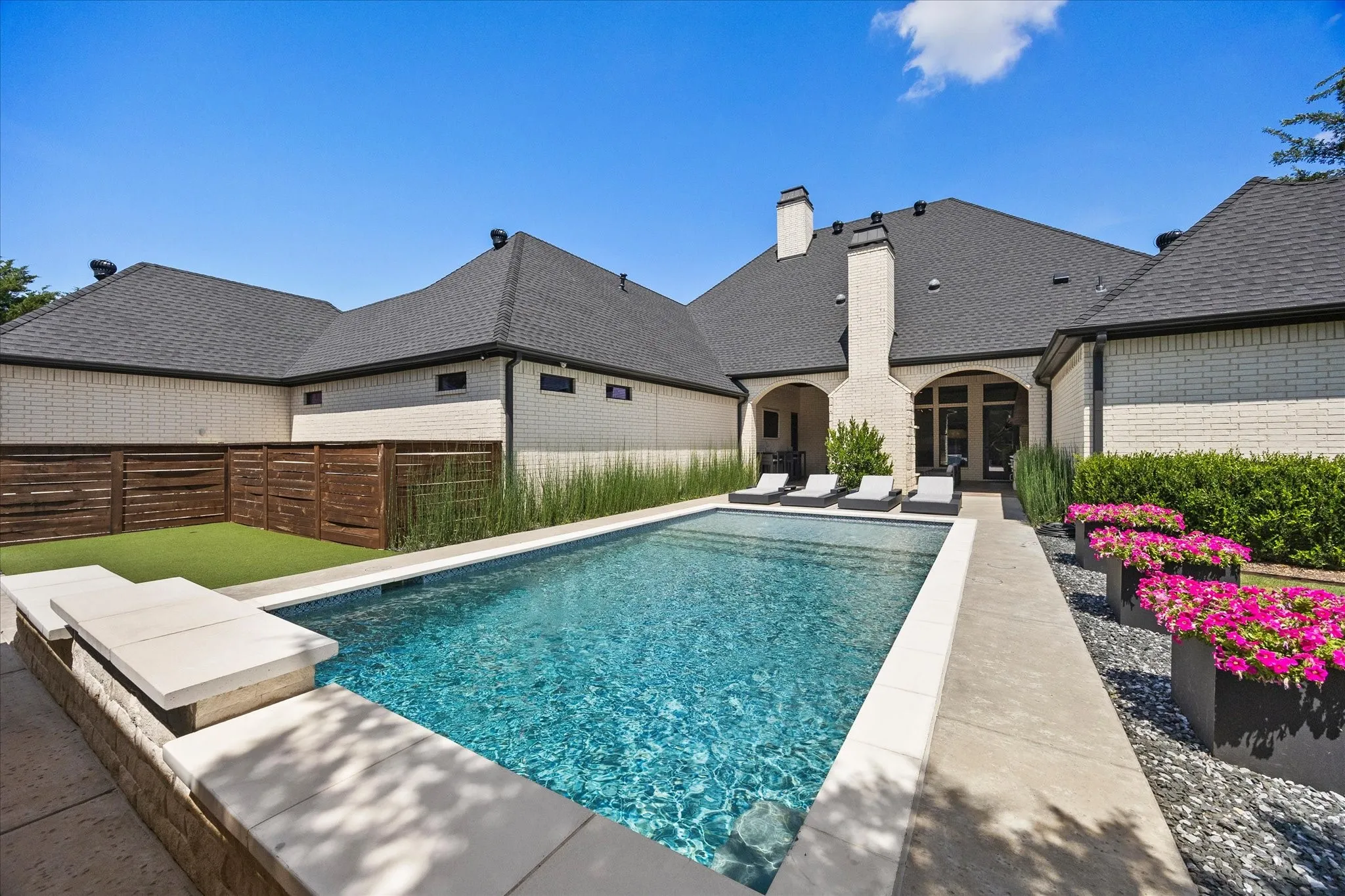 In-ground swimming pool, stone coping, concrete decking, brick exterior, and a wood privacy fence