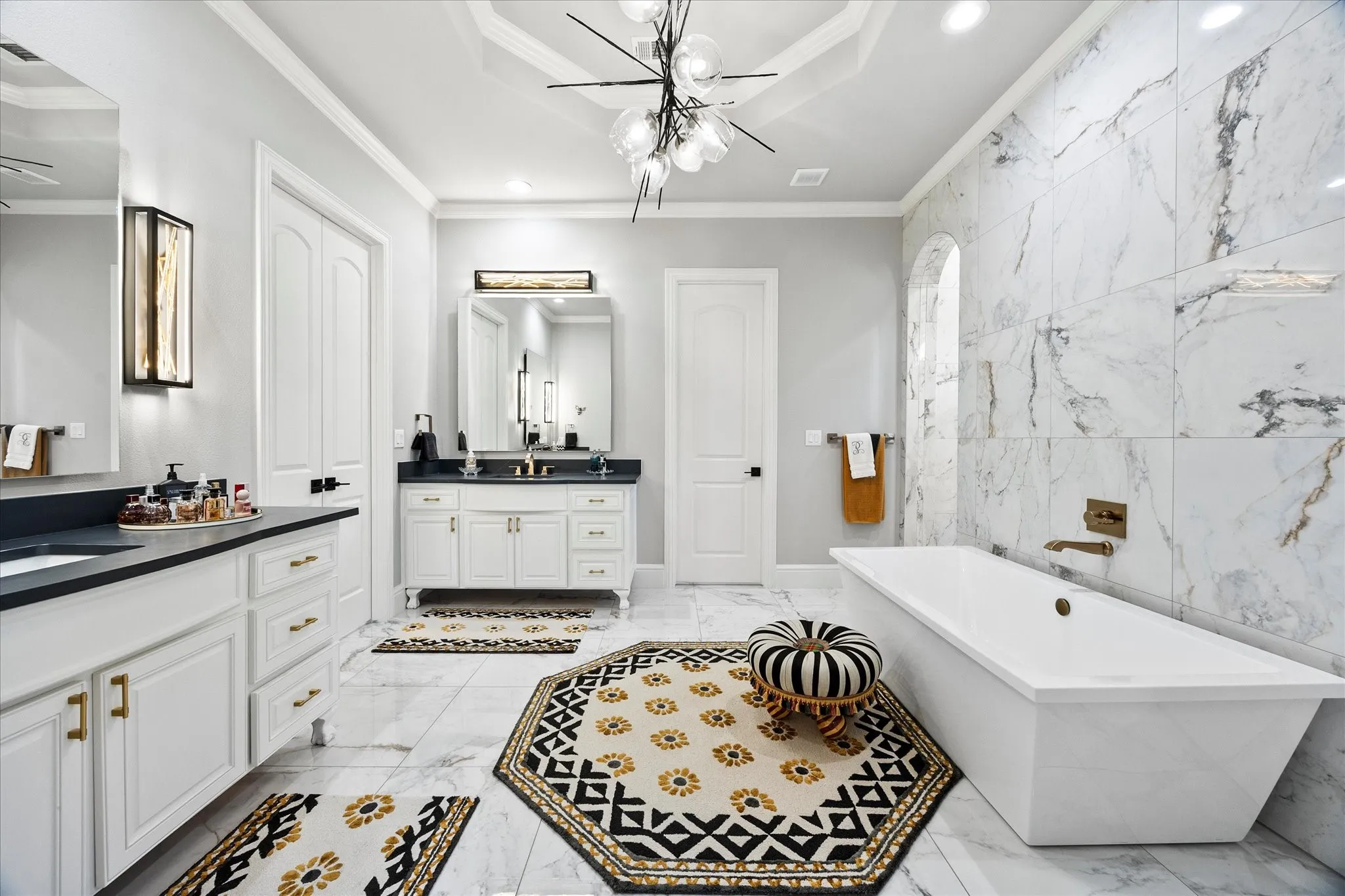 White freestanding bathtub with wall-mounted brass faucet, marble-look tile flooring, and a marble-look tiled accent wall featuring an arched alcove