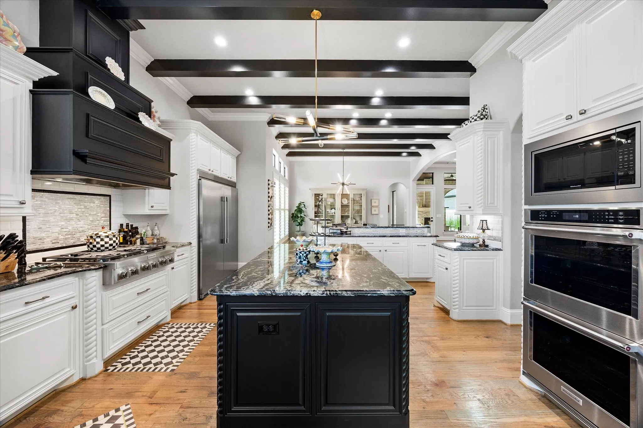 Gourmet kitchen featuring a large central island, white cabinetry, stainless steel appliances, wood-finish flooring, and exposed ceiling beams