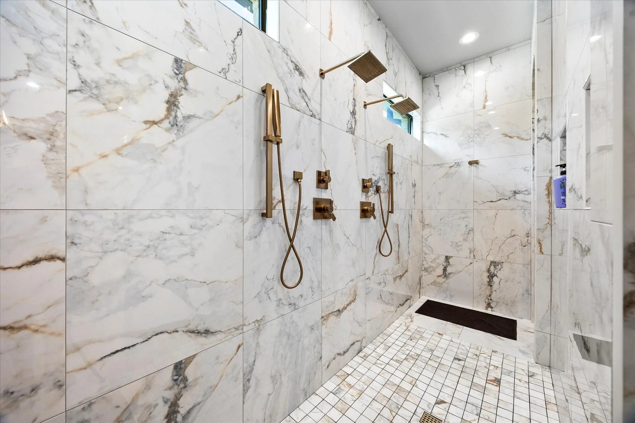 Spacious walk-in shower featuring large format tile walls, dual rain shower heads, dual handheld shower wands, and a mosaic tile floor