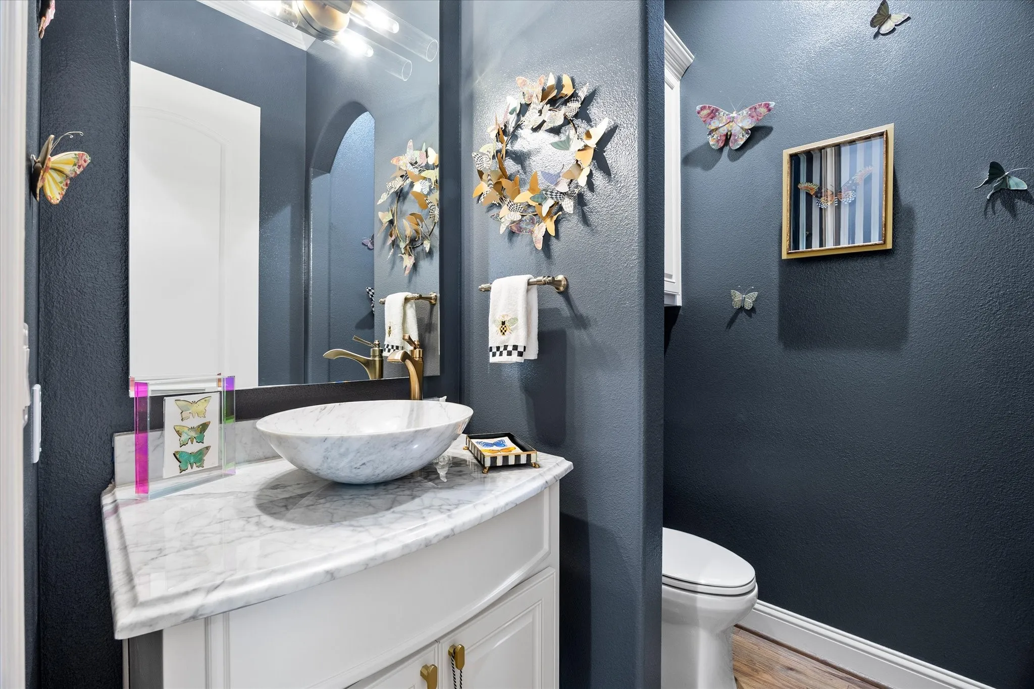 White vanity with gold-tone hardware, vessel sink, polished countertop, and wall-mounted mirror