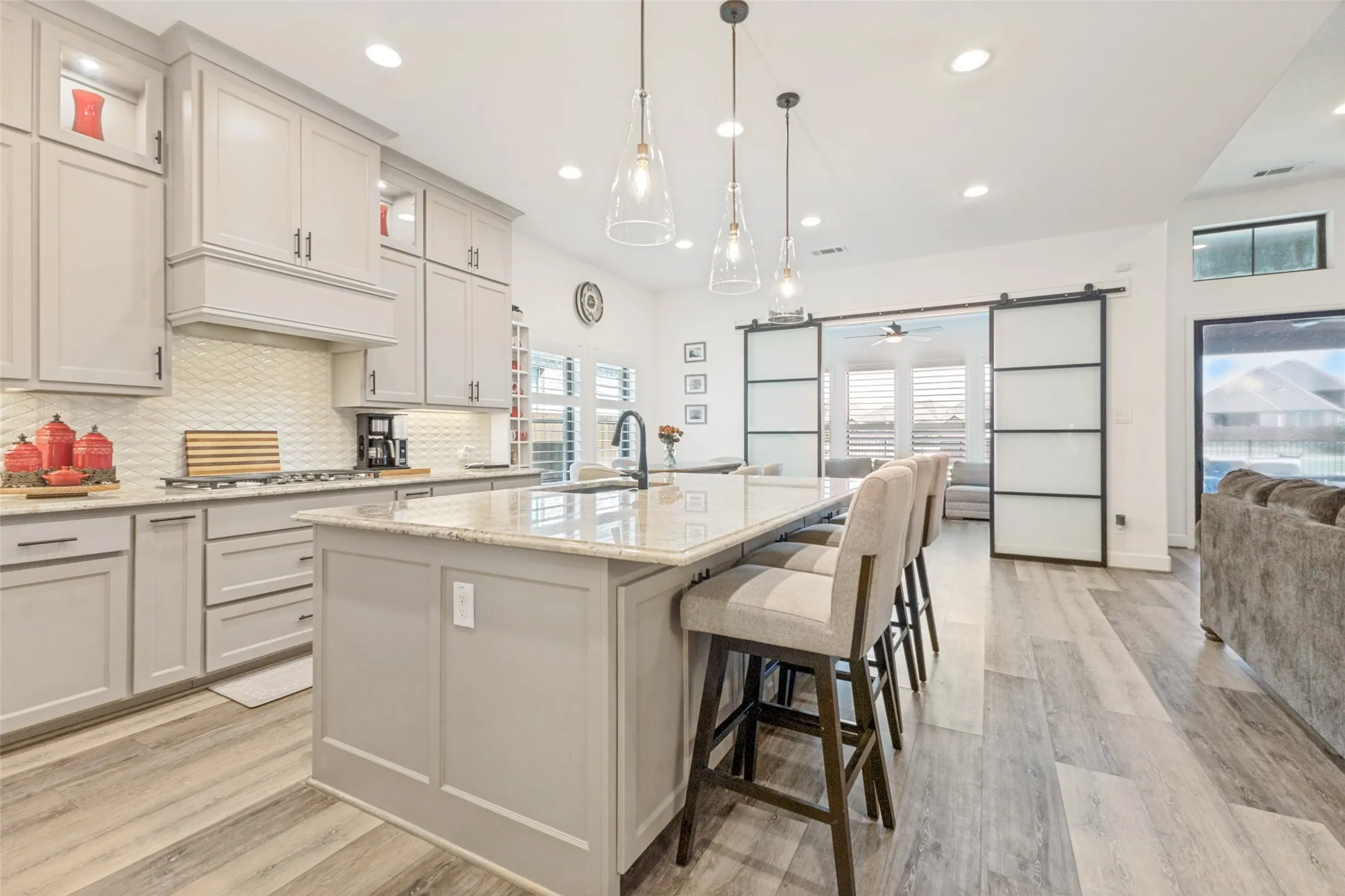 Open-concept kitchen featuring light-toned cabinetry, a large center island with a light-toned countertop, a cooktop with a decorative range hood, and wood-finish flooring