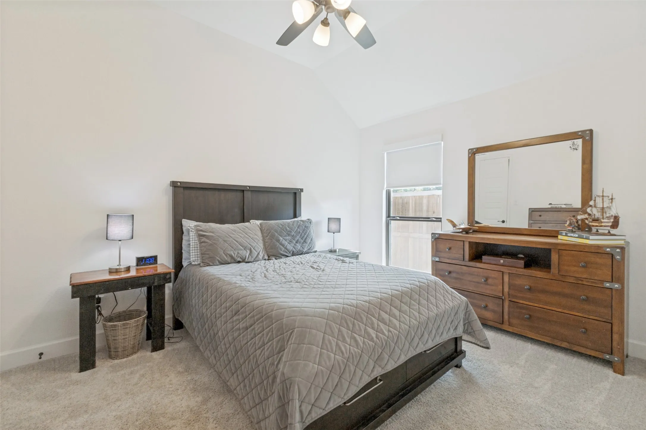 Vaulted ceiling, ceiling fan, carpeted flooring, window with roller shade, and light neutral wall paint