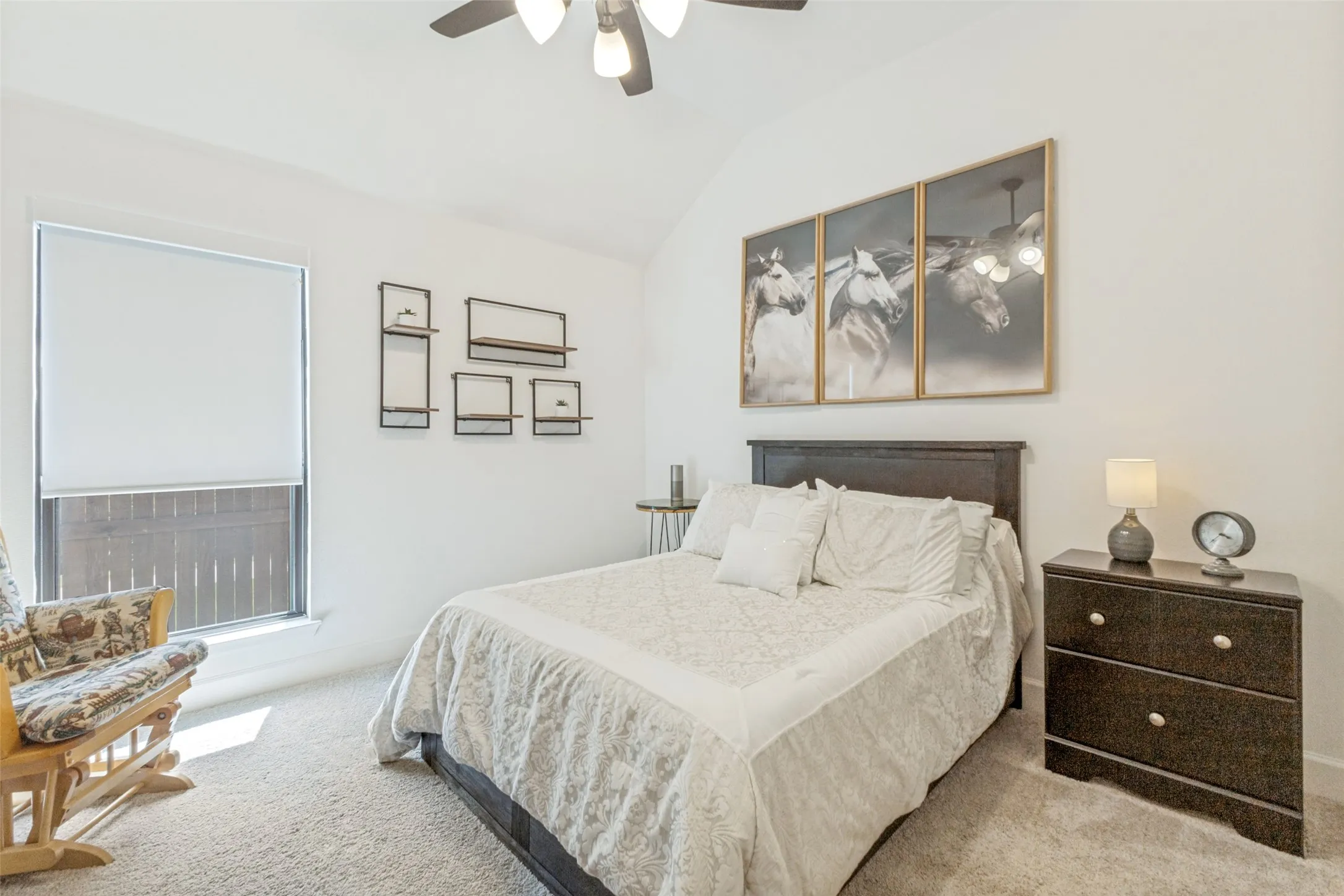 Vaulted ceiling with a ceiling fan, carpeted flooring, and a window with a roller shade