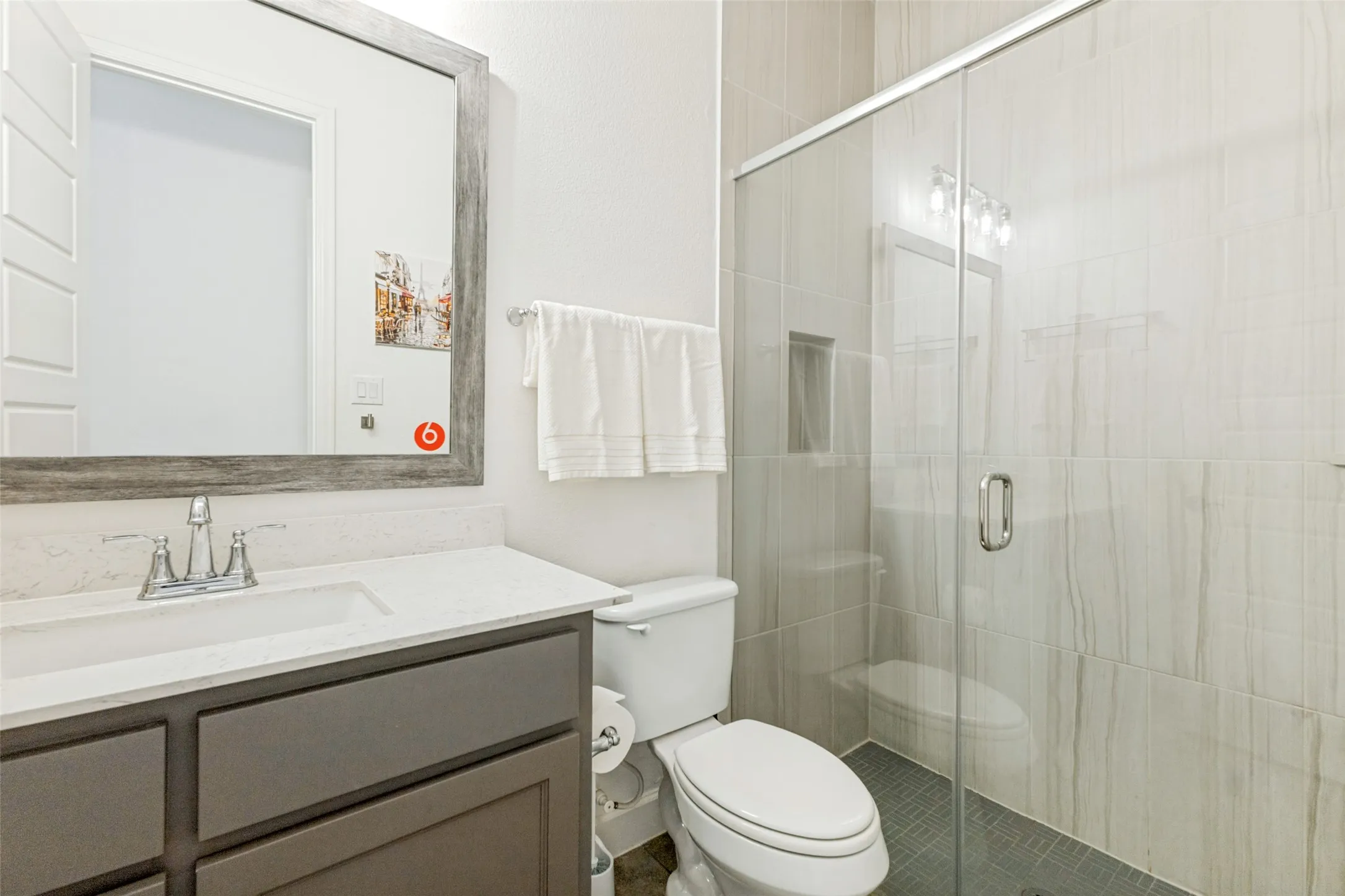 Vanity with a white countertop and undermount sink, framed mirror, glass-enclosed shower, shower niche, and tiled shower walls
