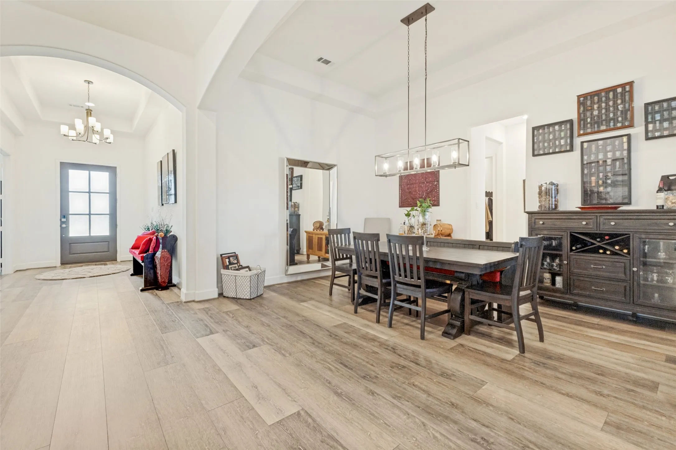 Wood-finish flooring throughout, arched entryway, tray ceiling, modern linear chandelier, and a built-in buffet with wine storage