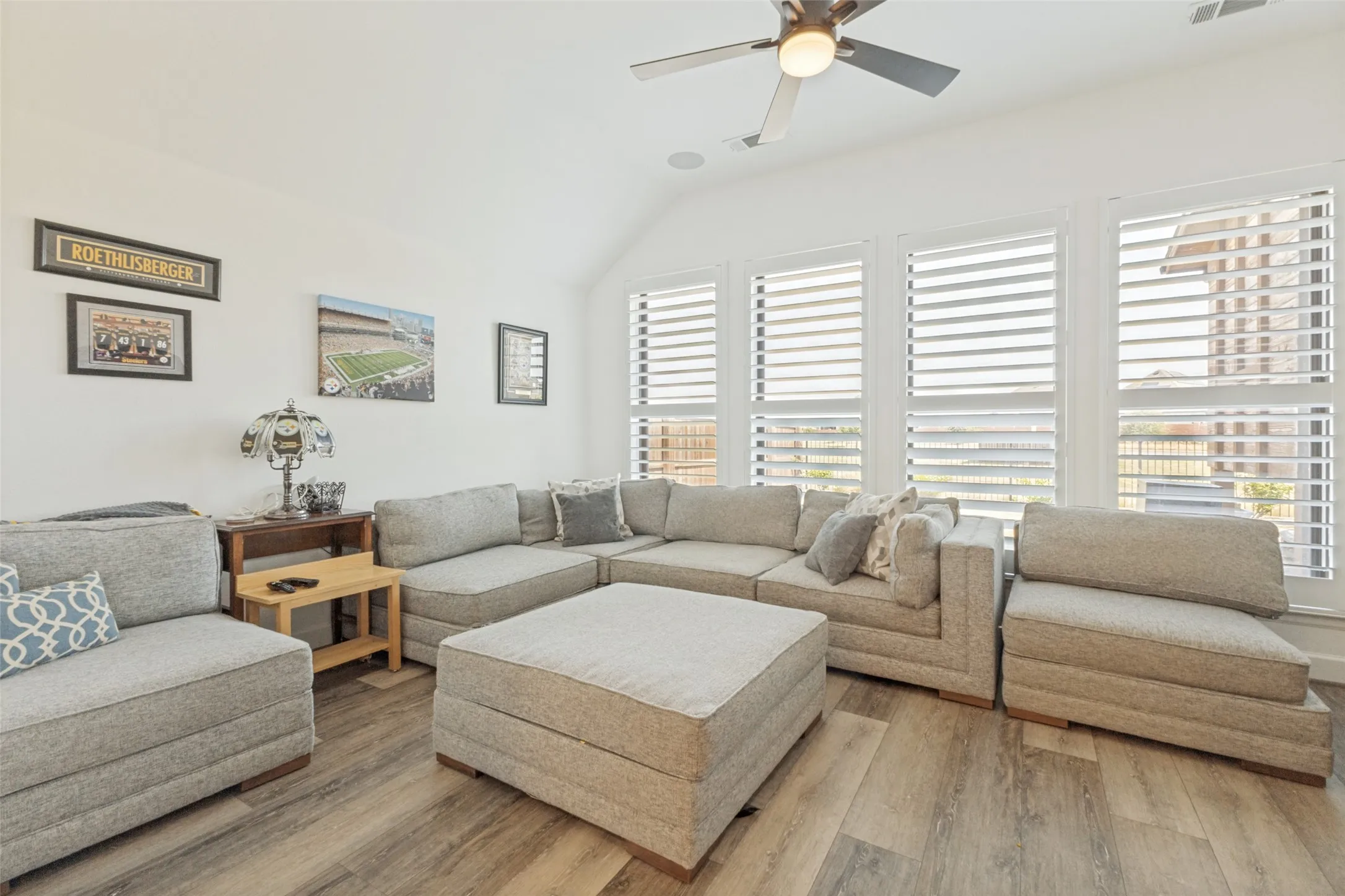 Vaulted ceiling with a ceiling fan, multiple windows with white plantation shutters, and wood-finish flooring
