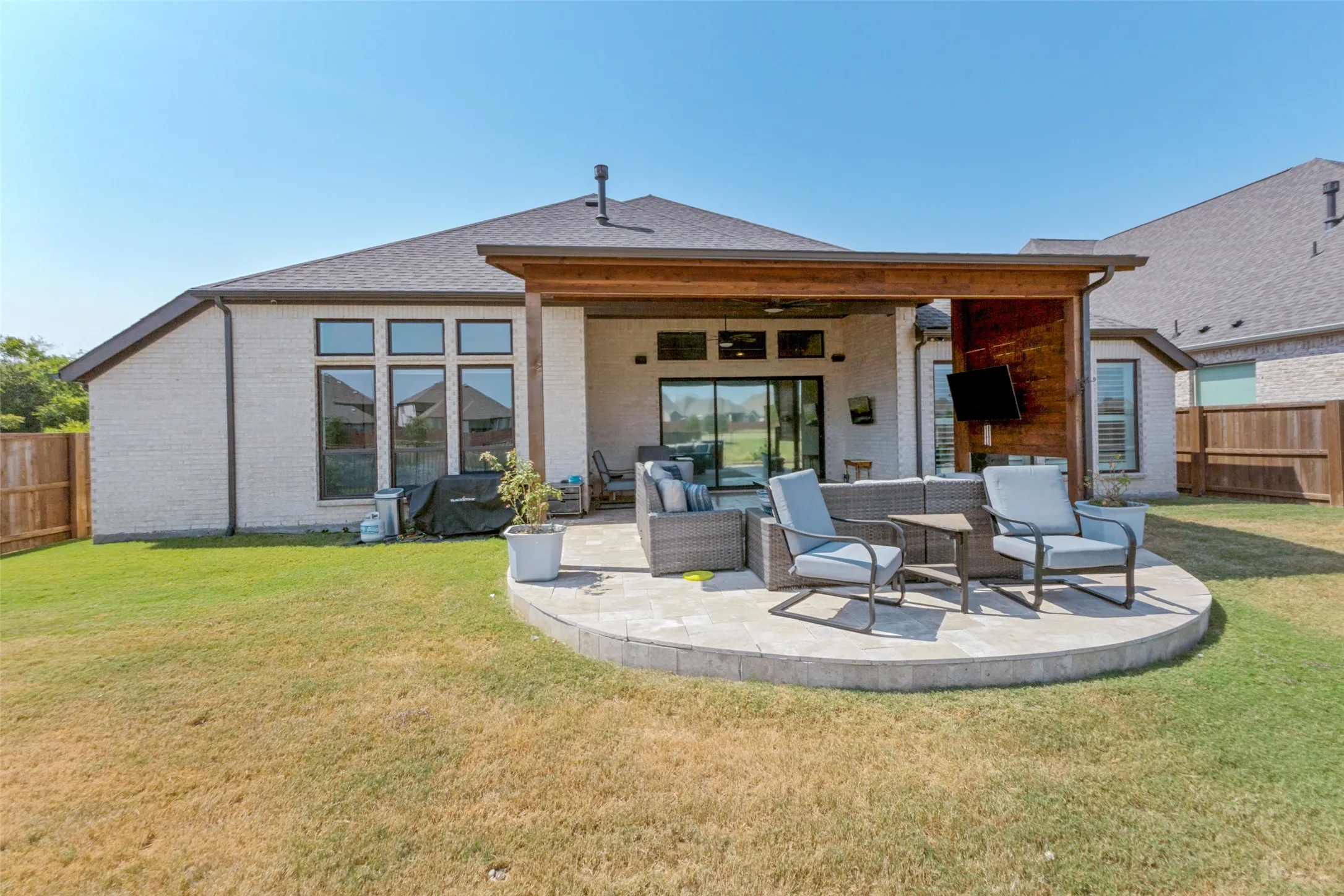 Covered patio with wood beam accents, brick exterior, large format sliding glass doors, and a paver patio