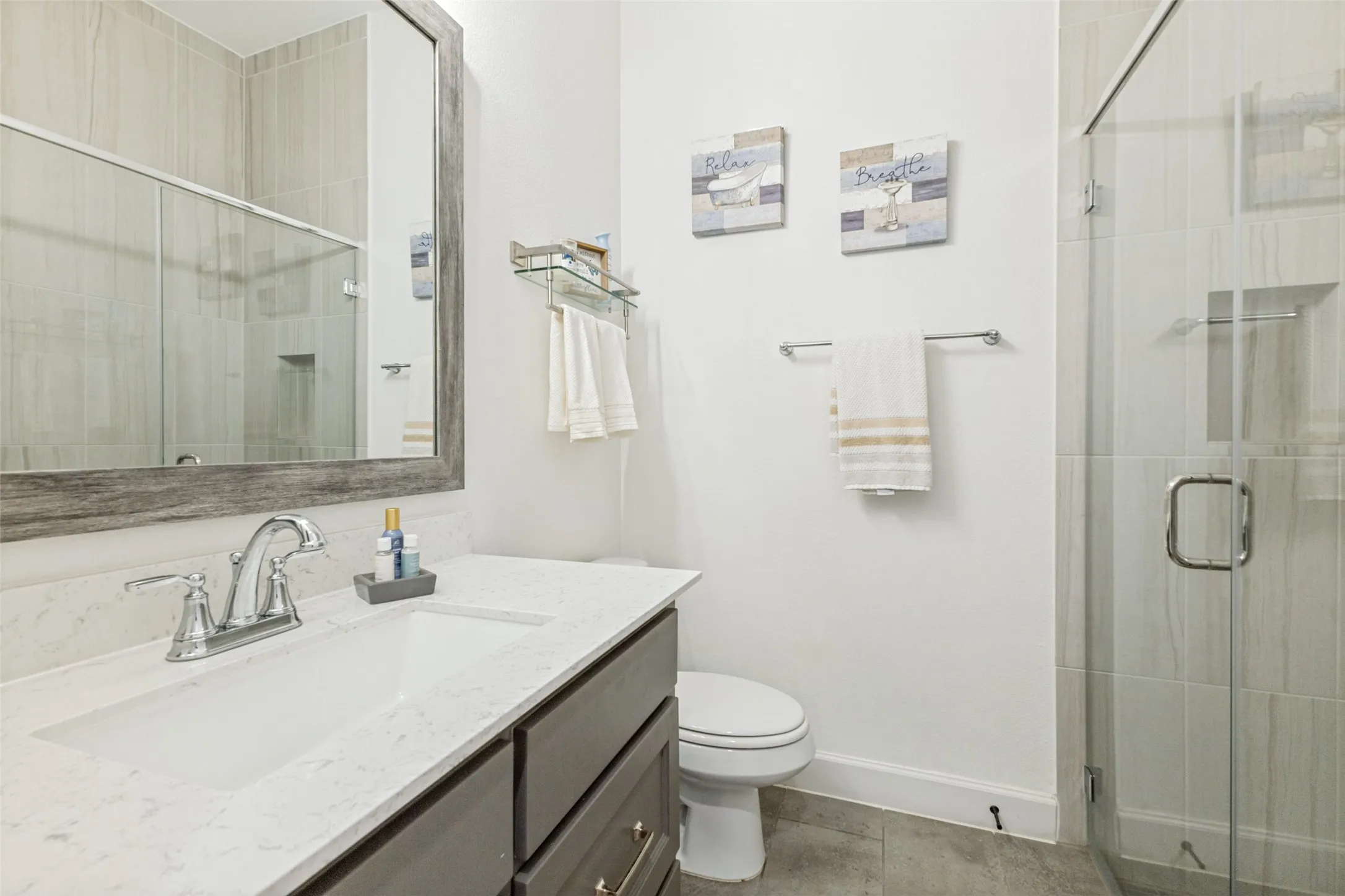 Vanity with an integrated rectangular sink and chrome faucet, framed mirror, glass-enclosed shower with tiled walls, and a built-in shower niche