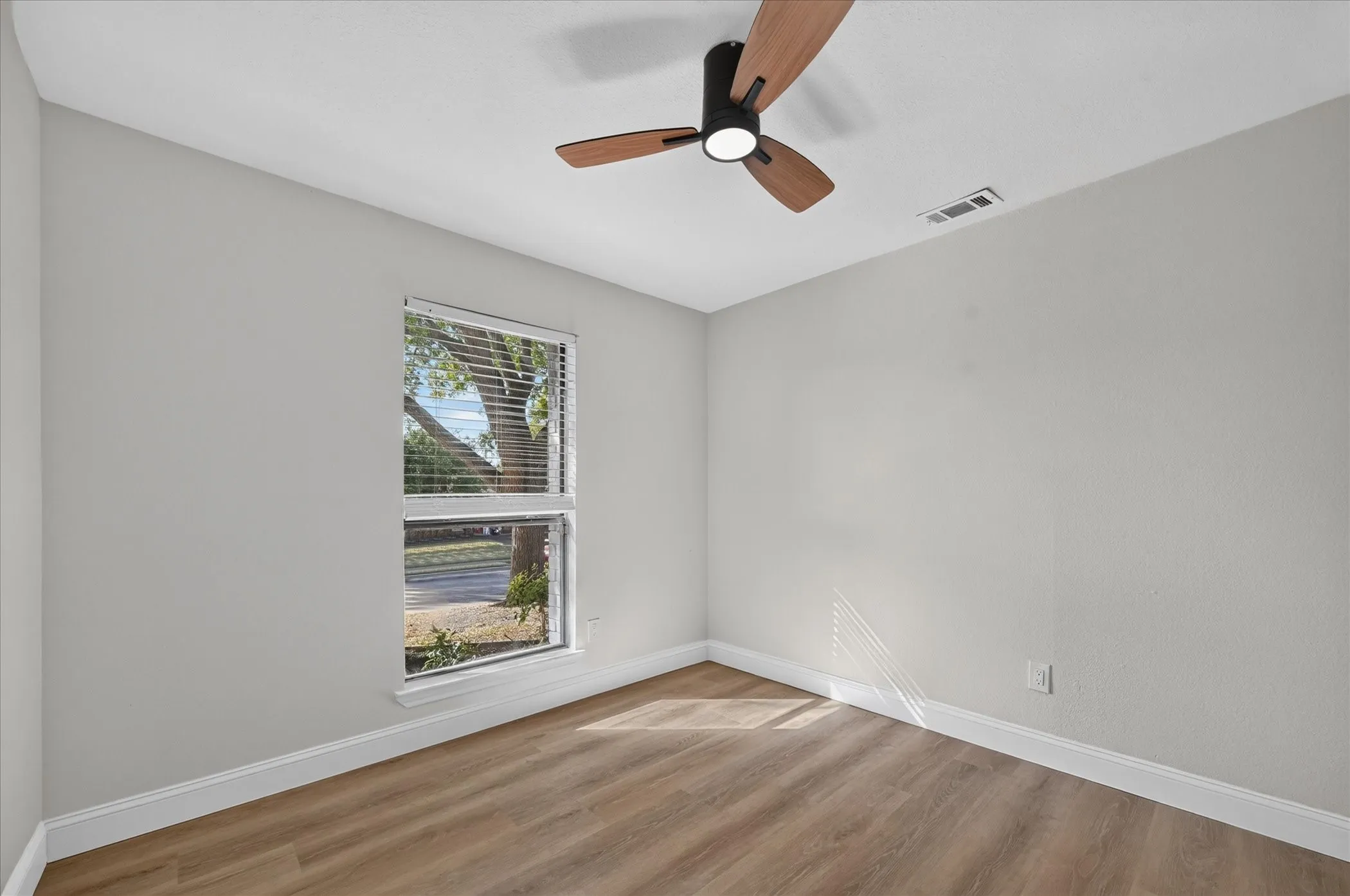 Wood-finish flooring, white trim, off-white walls, window with blinds, and a ceiling fan with light