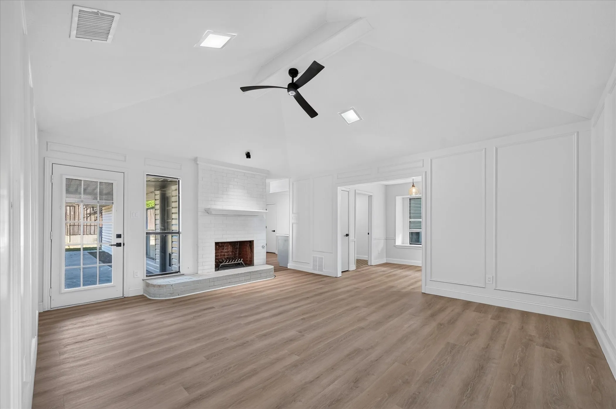 Vaulted ceiling with a ceiling fan, brick fireplace with a stone hearth, wood-finish flooring, accent wall paneling, and a full-light glass door