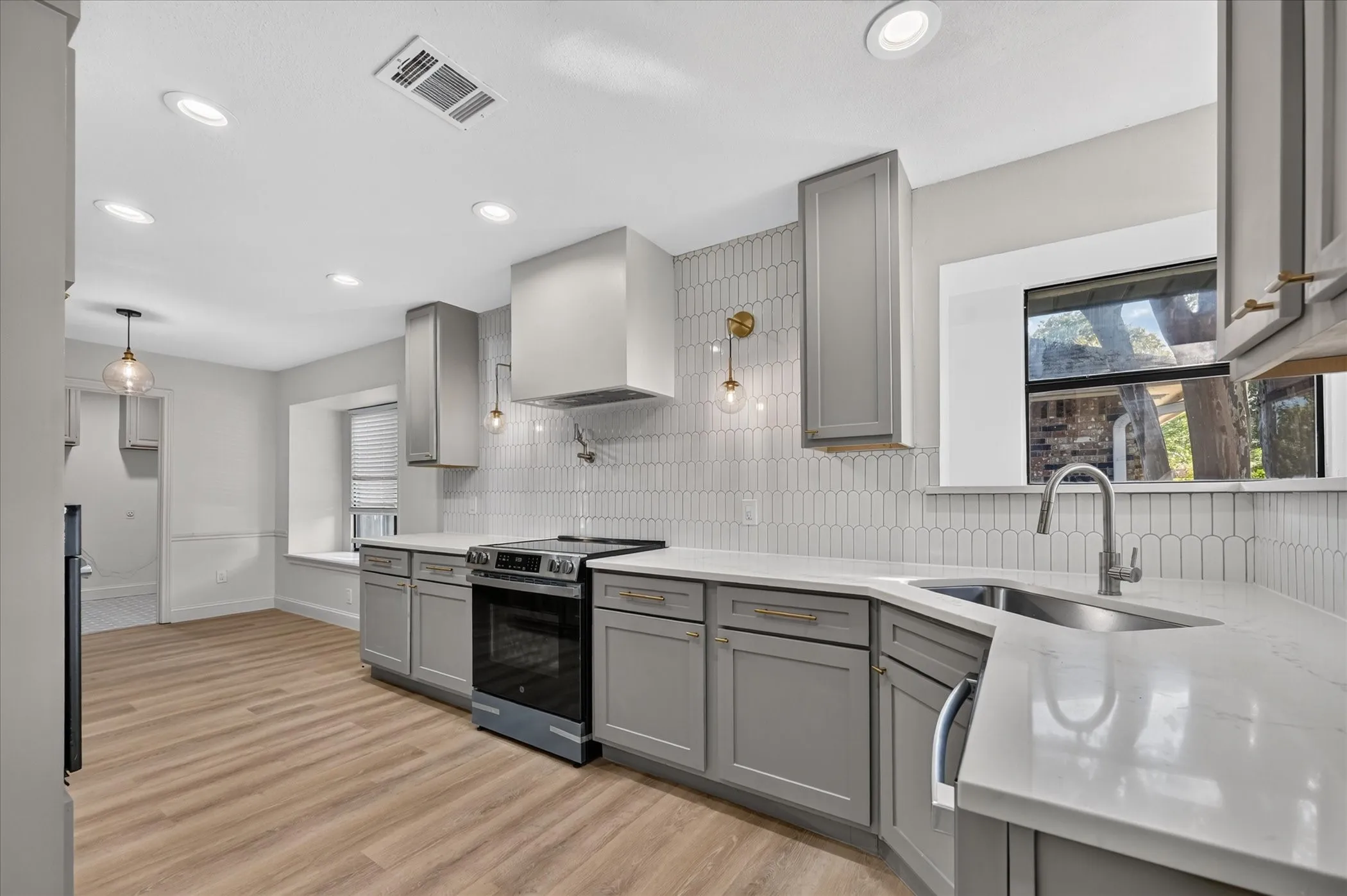 Kitchen featuring taupe cabinetry, white countertops, wood-finish flooring, a stainless steel range, and a white picket tile backsplash
