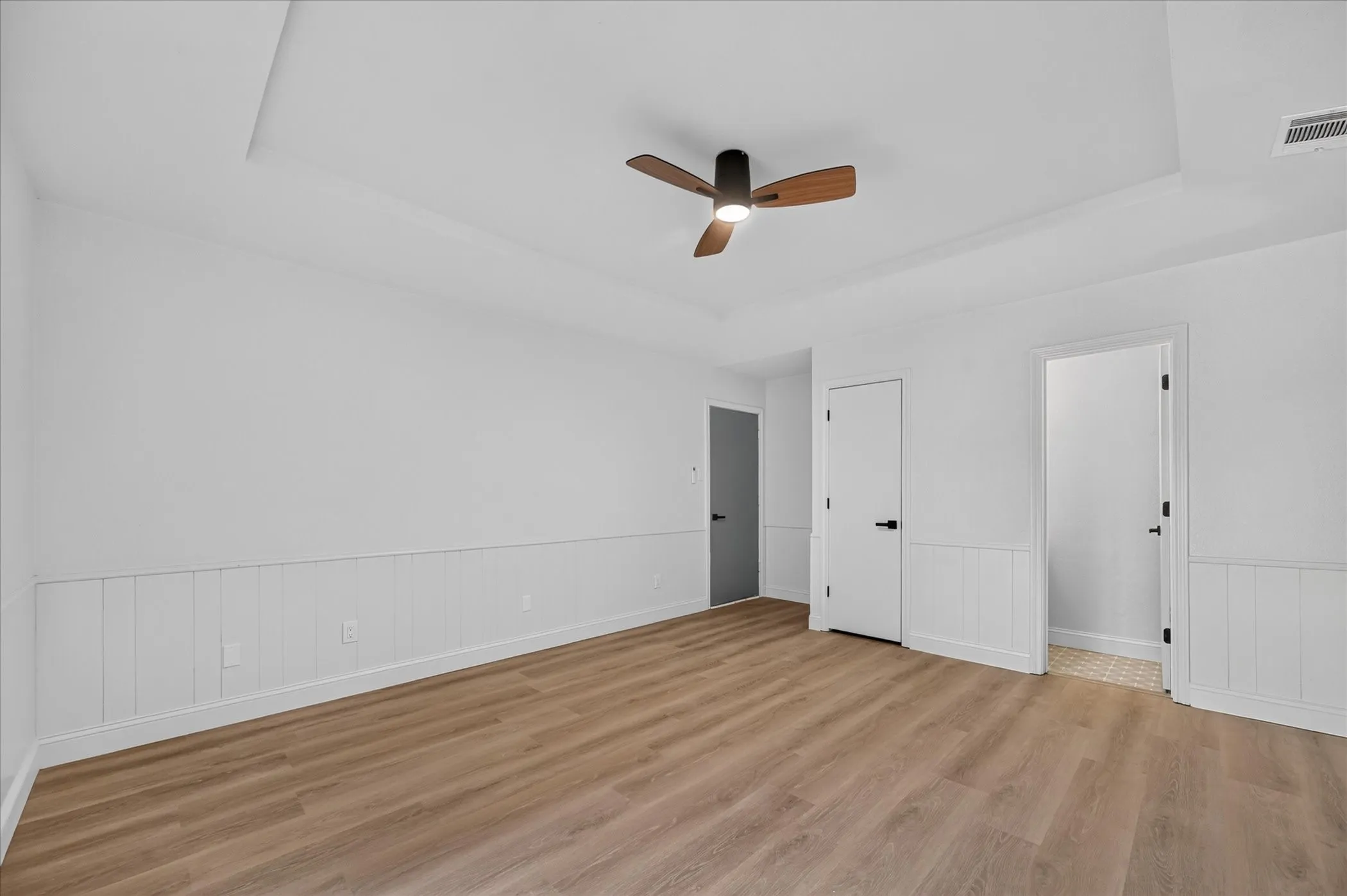 Tray ceiling, ceiling fan with wood-finish blades, wood-finish flooring, white wainscoting, white doors with matte black hardware