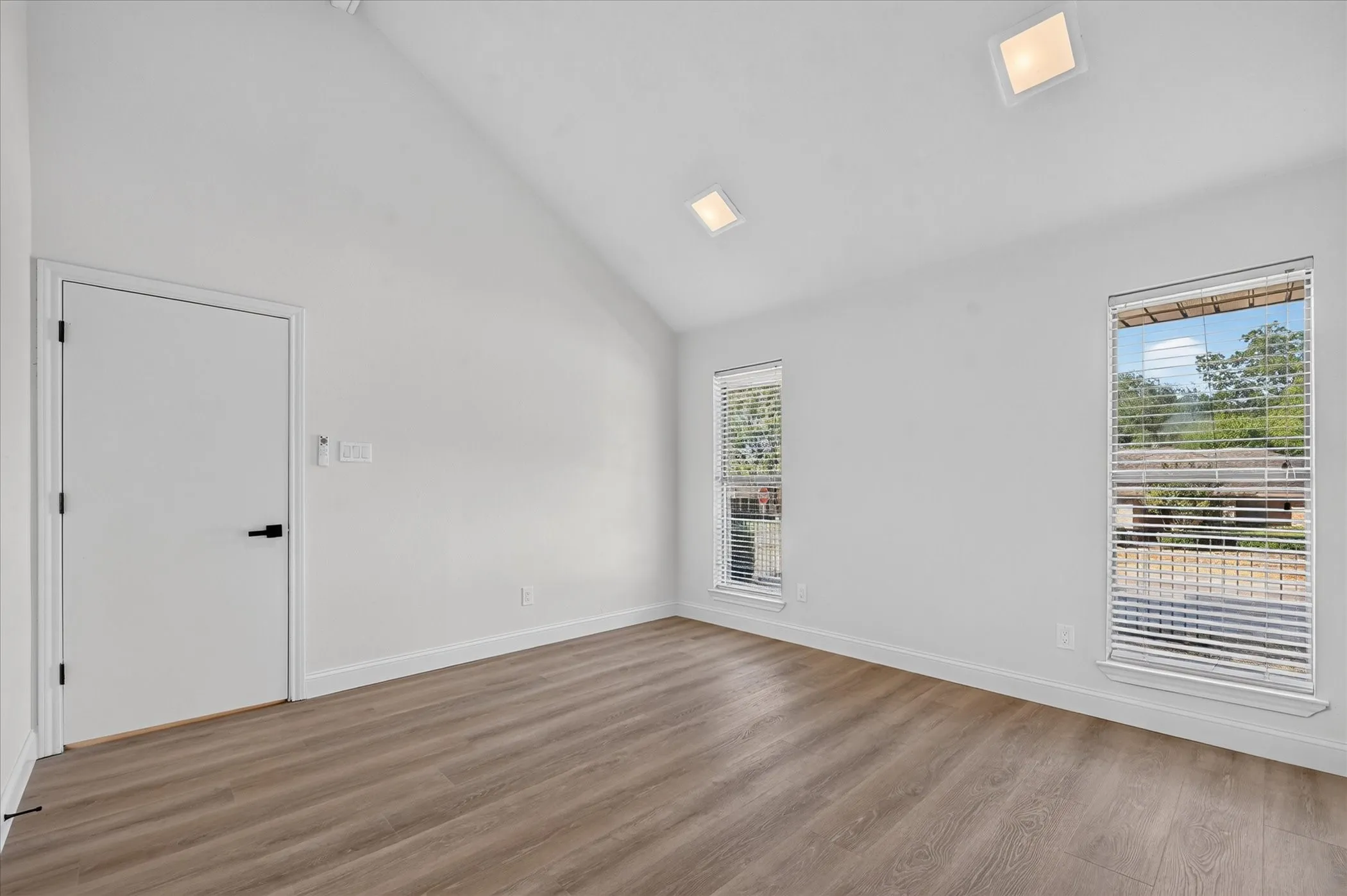Vaulted ceiling, wood-finish flooring, recessed lighting, and two windows with blinds