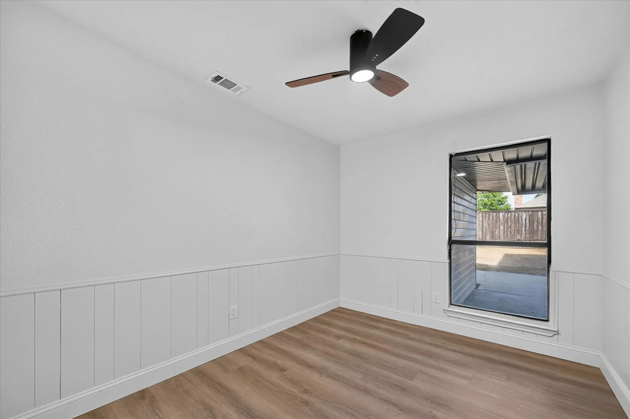 Recessed window with black trim, wood-finish flooring, white paneled wainscoting, and a contemporary ceiling fan with integrated lighting