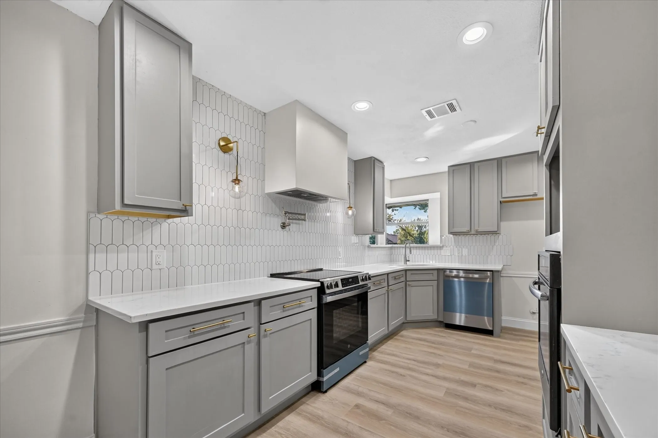 Kitchen featuring taupe cabinetry, white countertops, wood-finish flooring, a stainless steel range, and a white picket tile backsplash