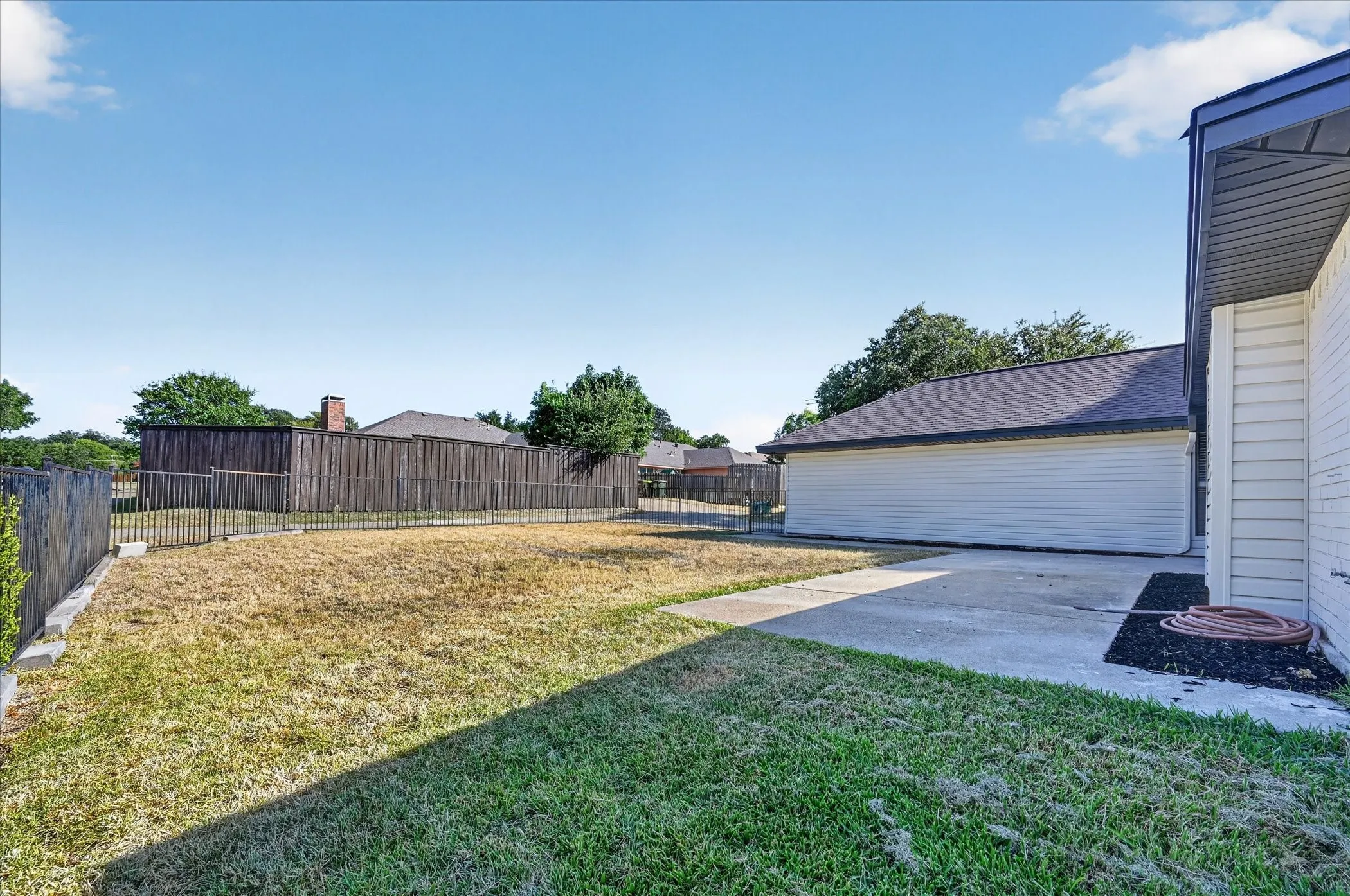Expansive backyard featuring a partial wood privacy fence, partial metal fencing, concrete patio, and mature trees