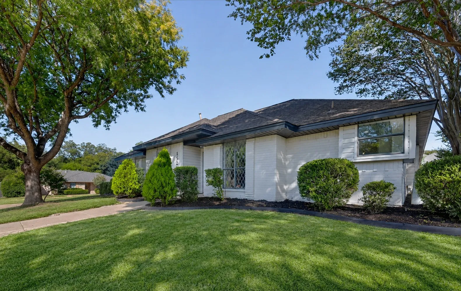 White brick exterior with a dark roof and manicured landscaping