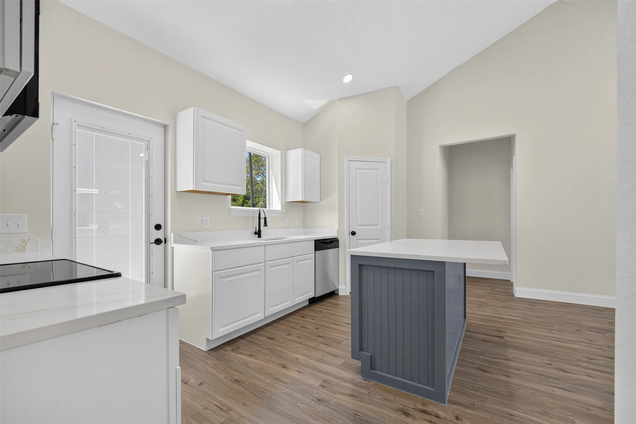 Kitchen featuring vaulted ceilings, white cabinetry, a built-in cooktop, an undermount sink with a black faucet, and a gray kitchen island with a countertop extension