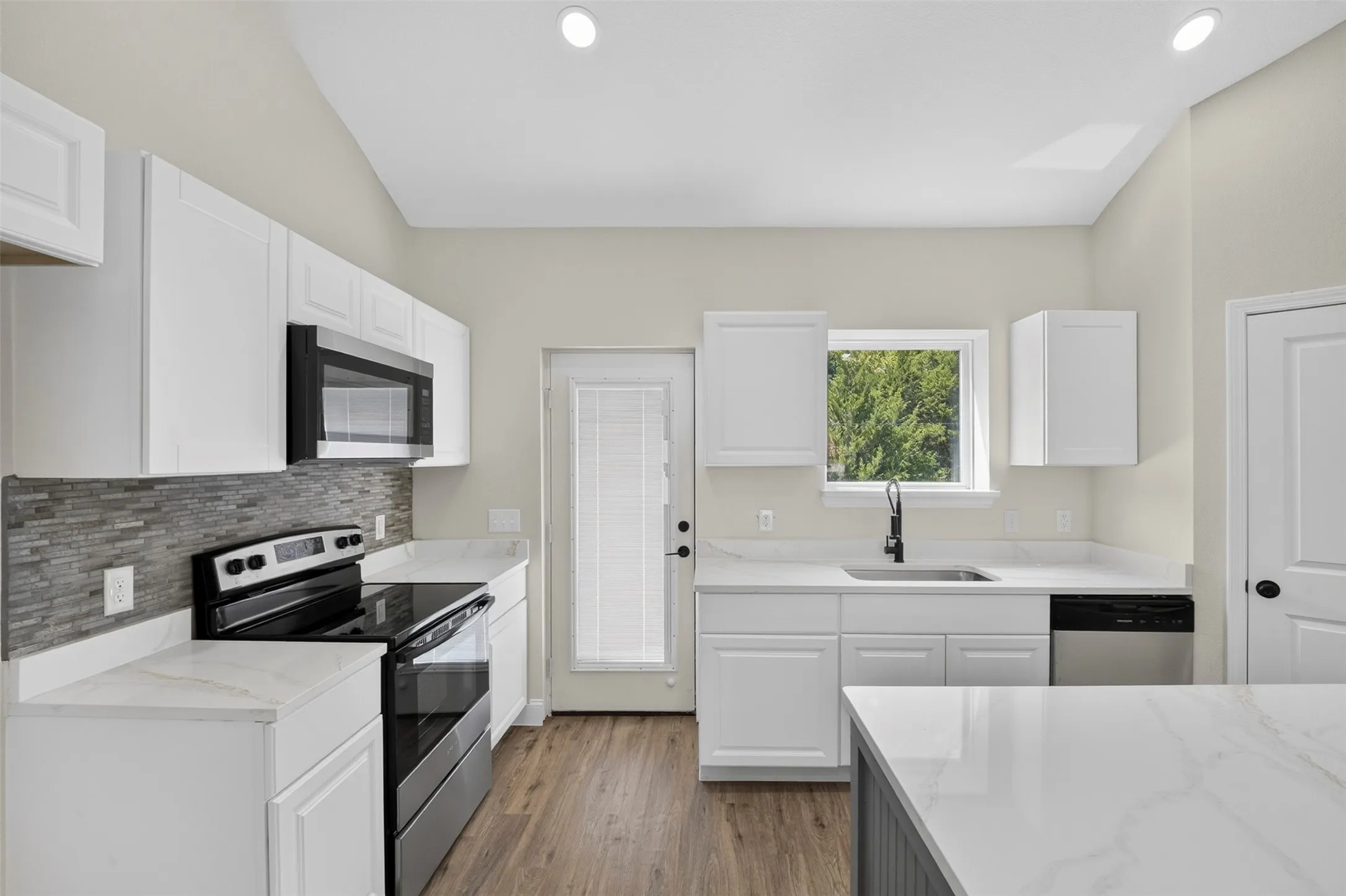 White shaker cabinetry with stone-finish countertops, stainless steel appliances, wood-finish flooring, and a tile backsplash