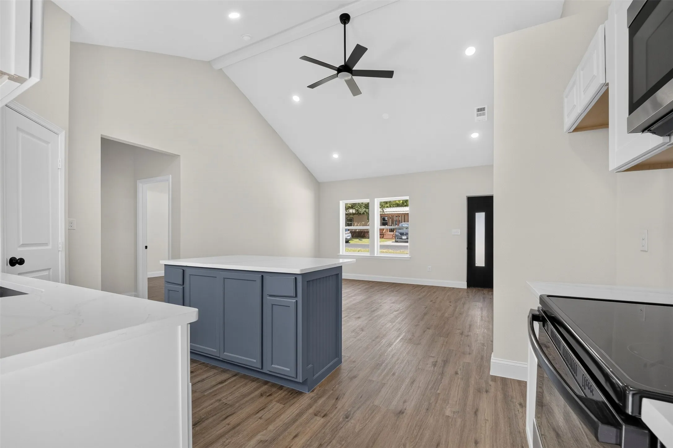 Vaulted ceilings, wood-finish flooring, recessed lighting, kitchen island with built-in storage, and modern ceiling fan