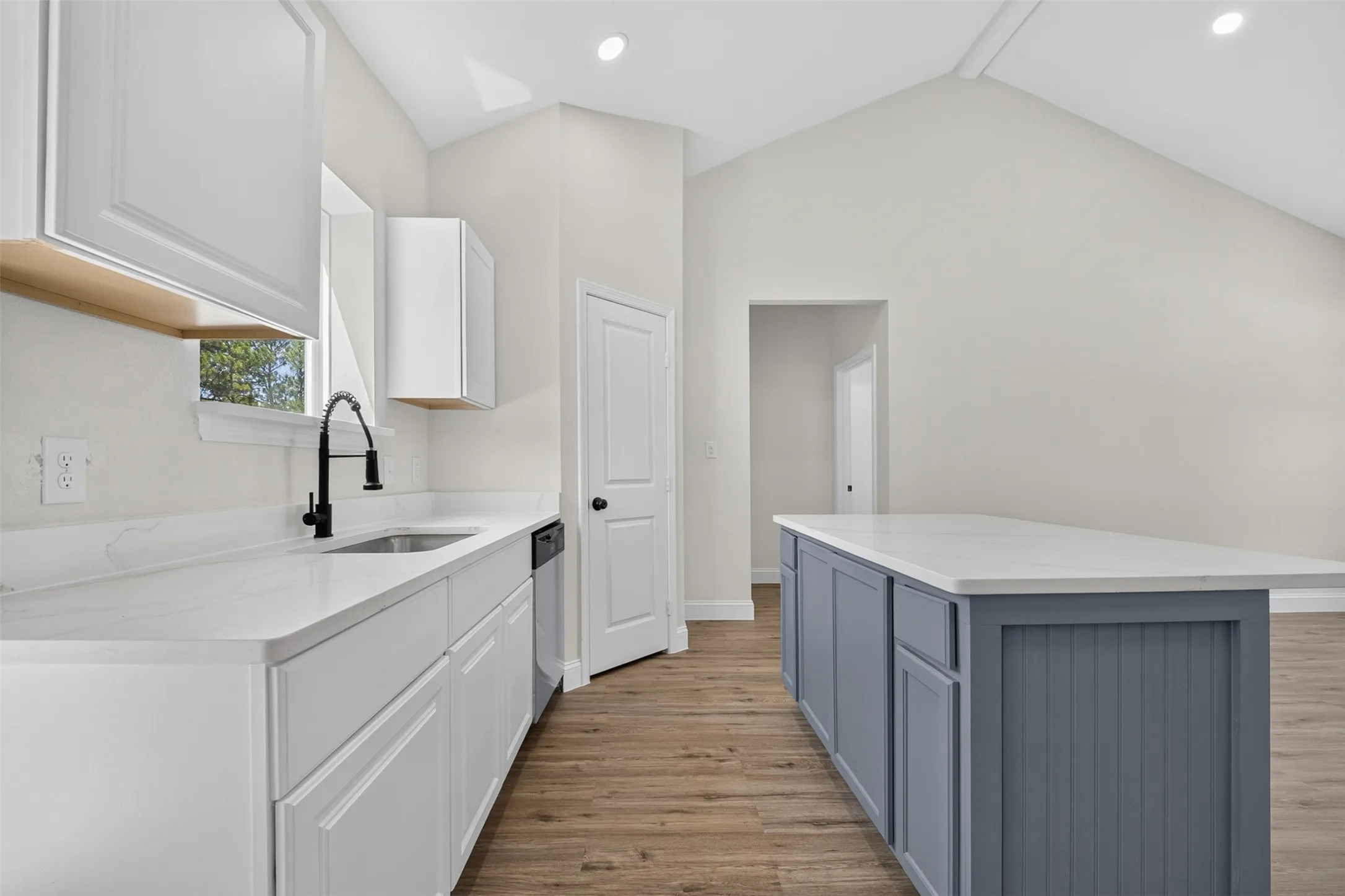 Vaulted ceiling, wood-finish flooring, white cabinetry, solid surface countertops, and a kitchen island with beadboard paneling